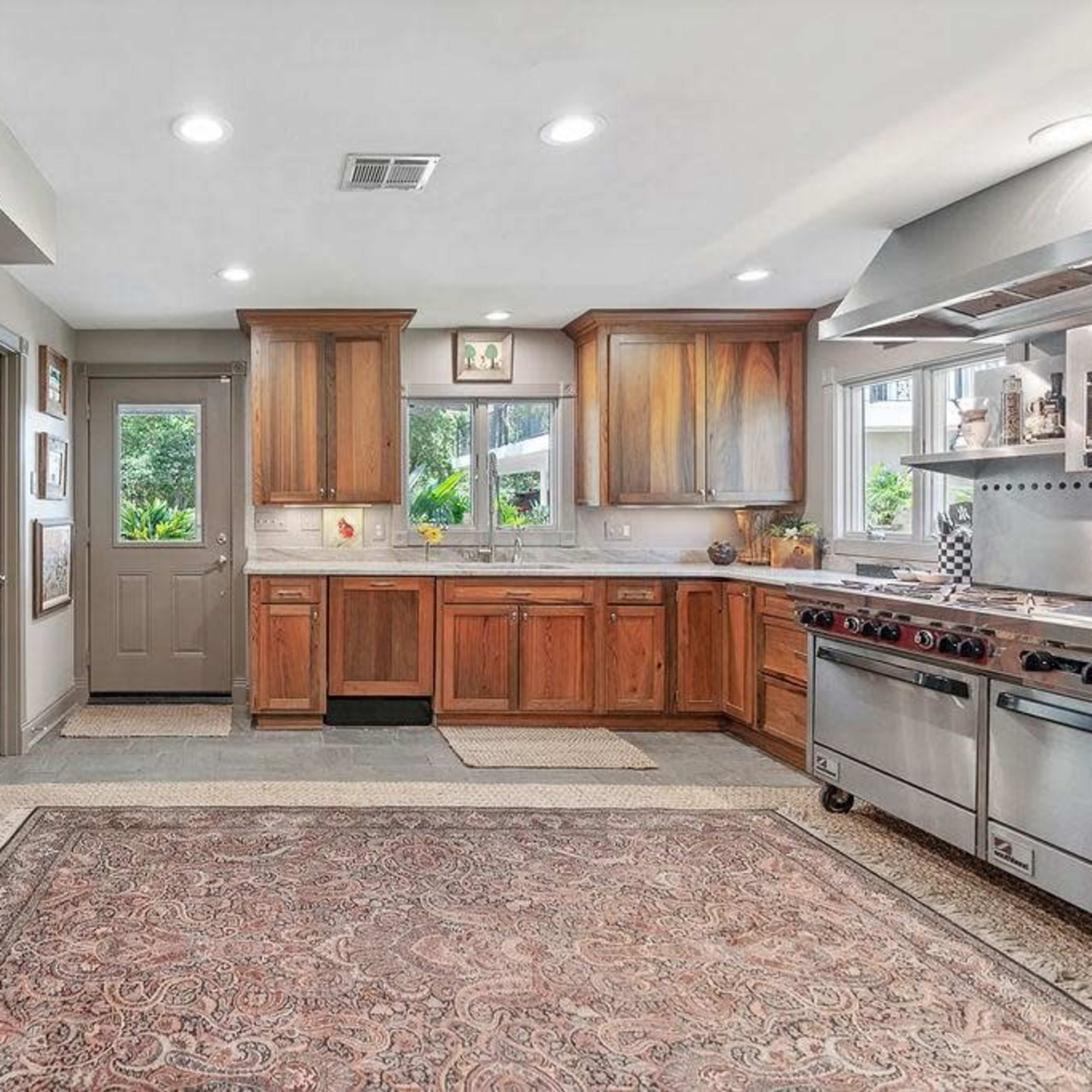 A spacious kitchen features wooden cabinetry, stainless steel appliances, and a large area rug.