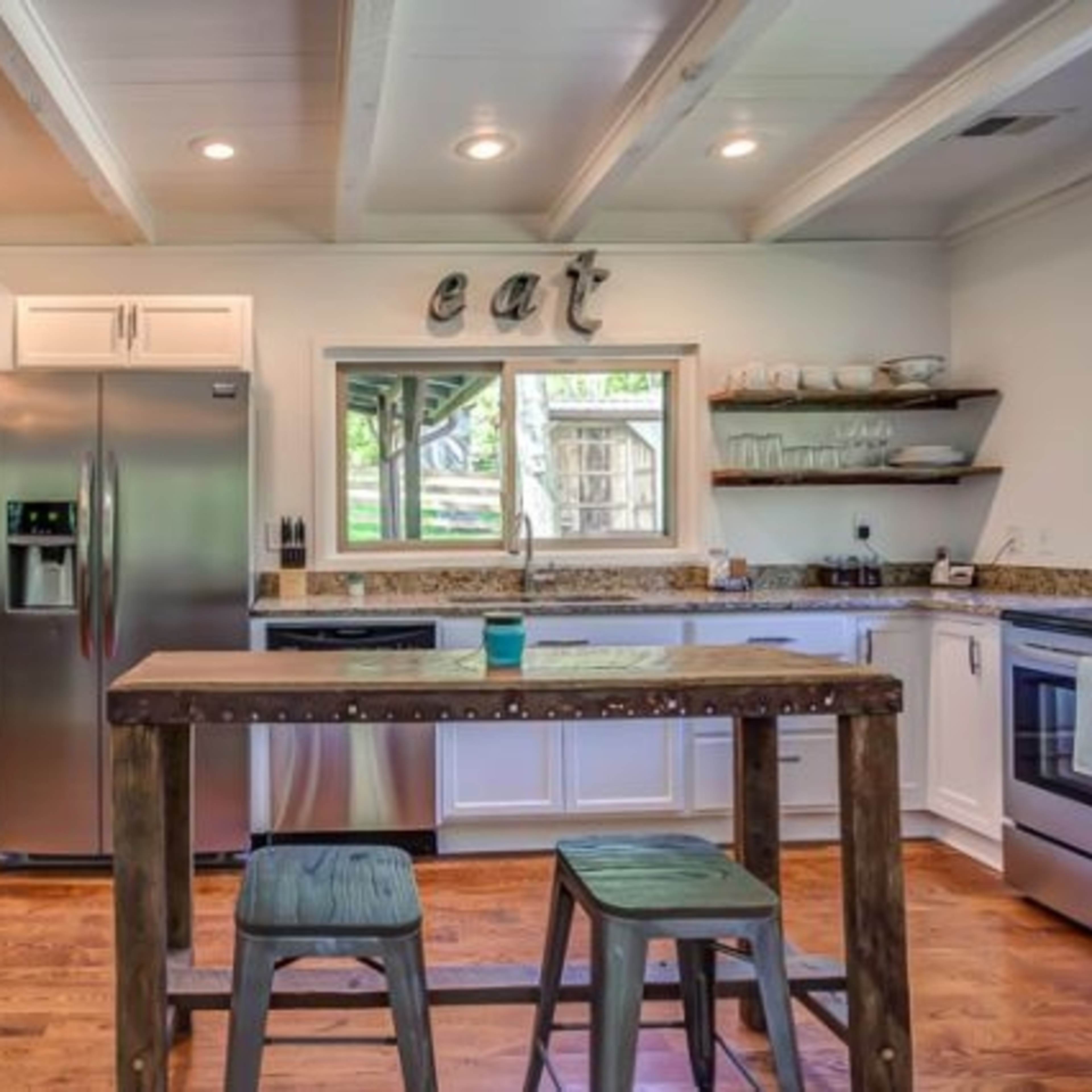 A modern kitchen features stainless steel appliances, wooden accents, and a counter with stools.