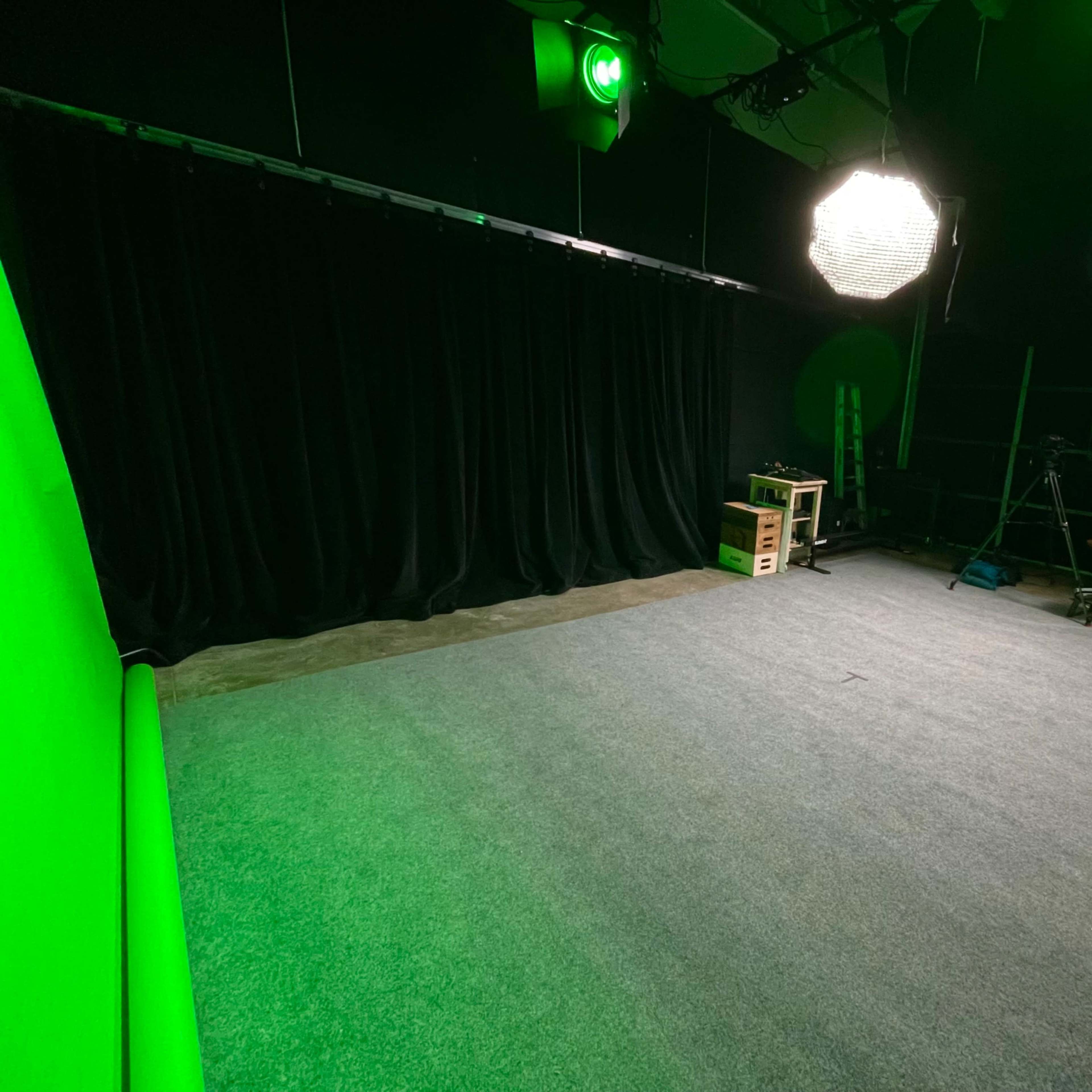 An empty studio space with a green screen backdrop, softbox lights, and a carpeted floor.