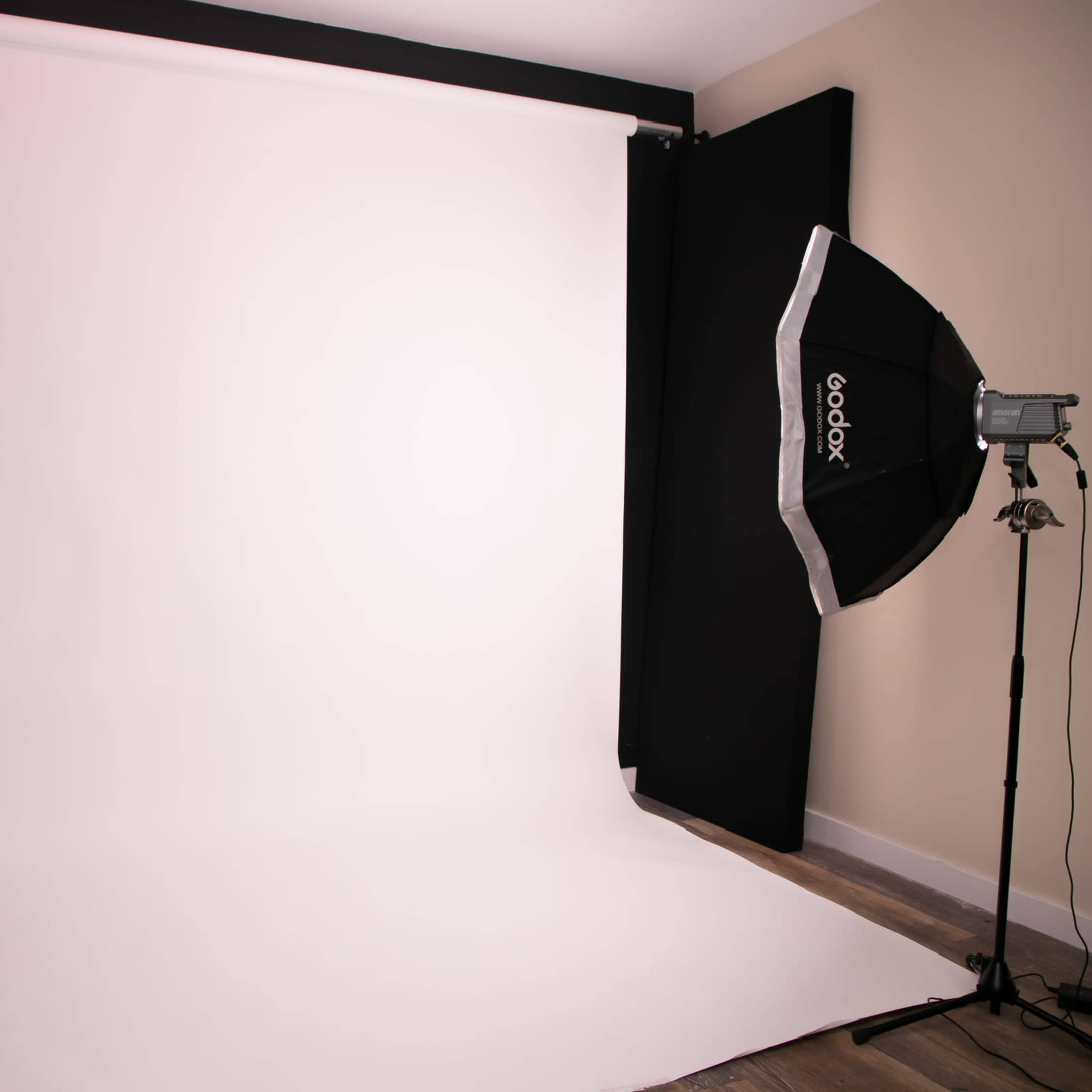 A photography studio with a large white backdrop and a lighting setup on the side.