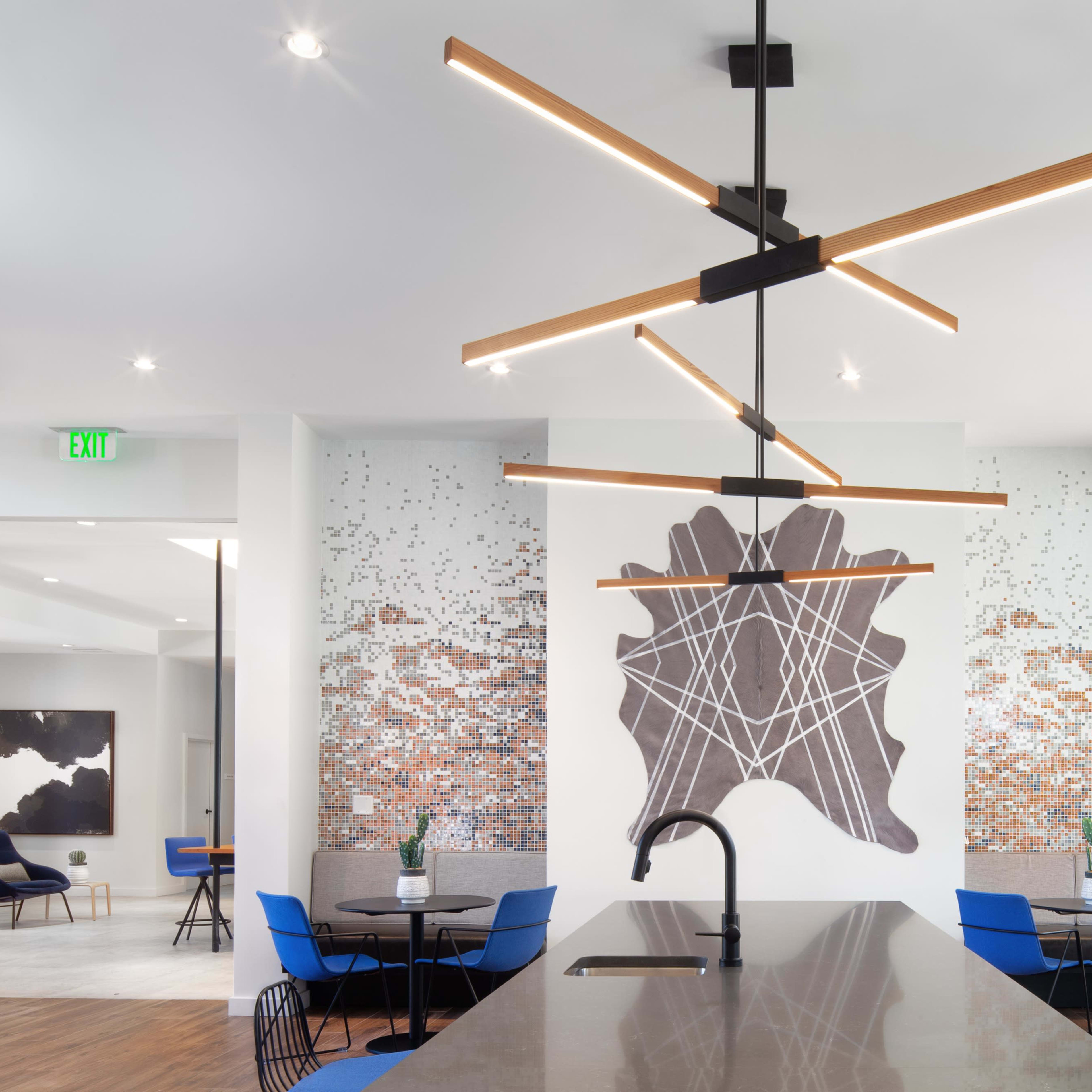 A modern dining area with a large island countertop, contemporary lighting fixtures, and a mural of abstract shapes on the wall.