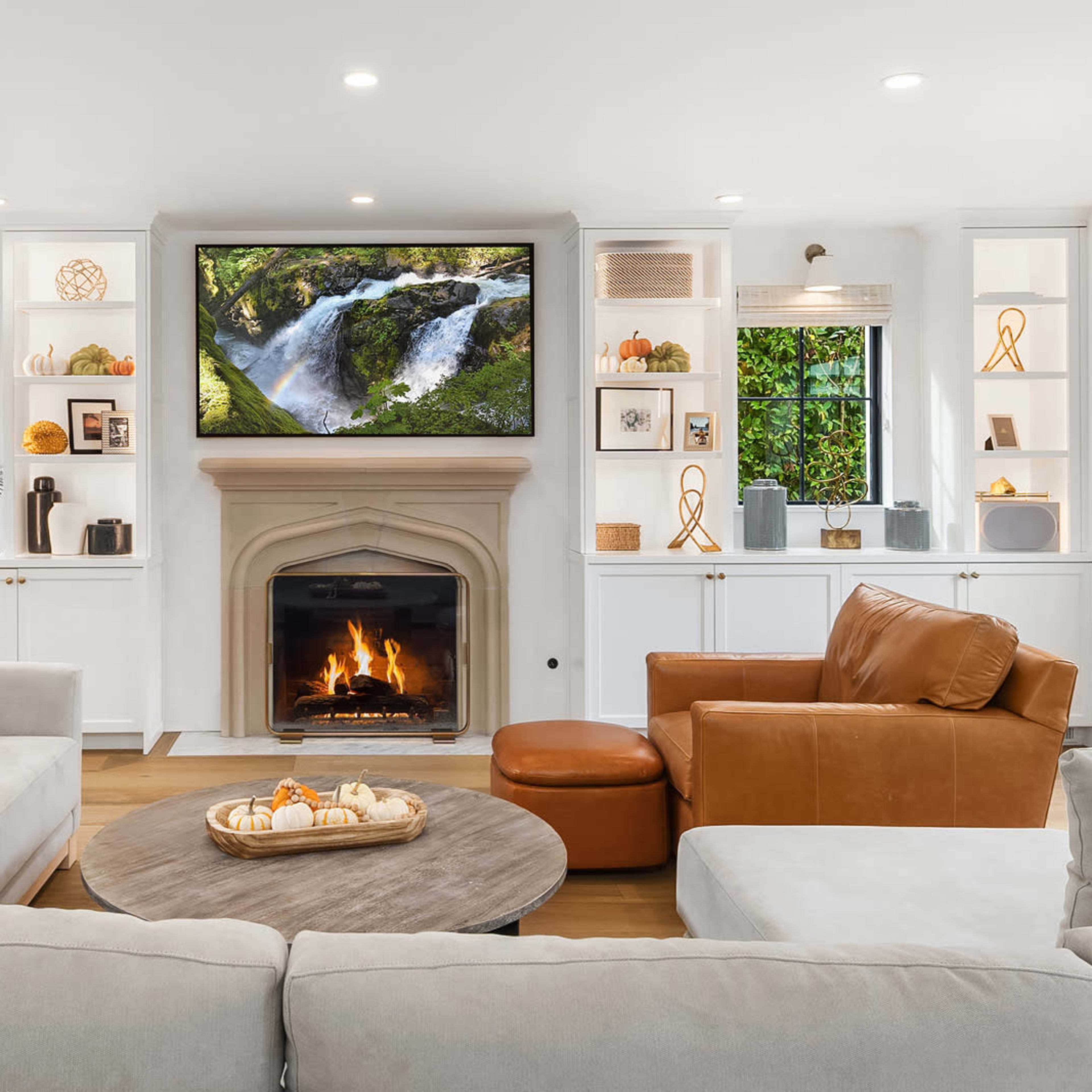 A cozy living room features a fireplace, a large TV mounted above it, and built-in shelves with decorative items.