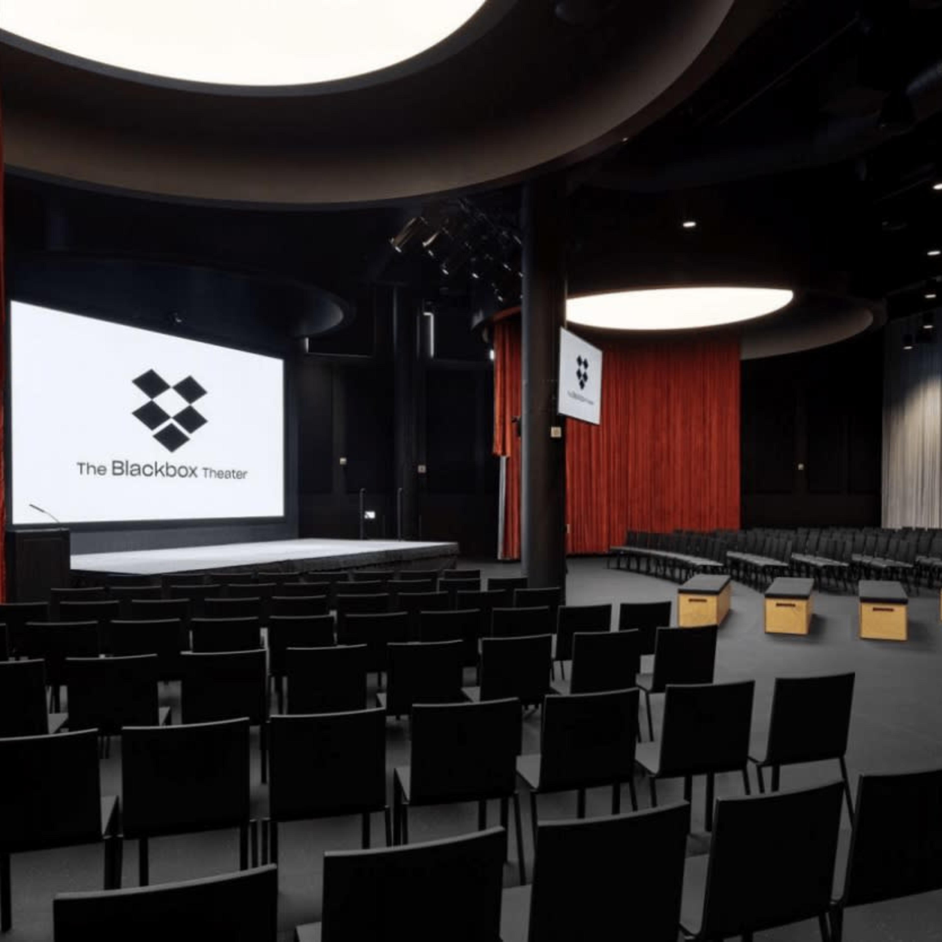 A modern theater space with rows of black chairs facing a large screen, flanked by red curtains.