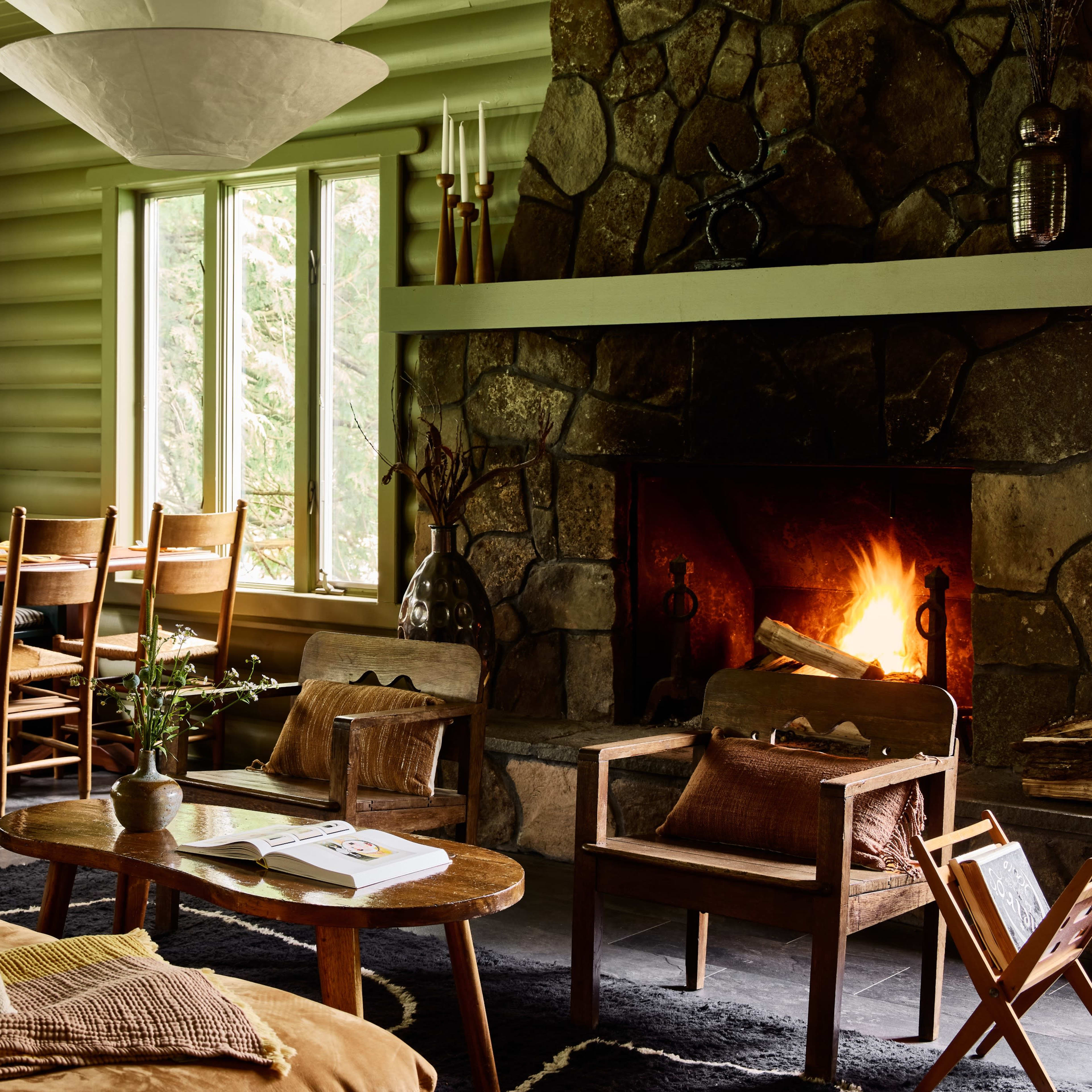 A cozy living room with a stone fireplace, wooden furniture, and large windows allowing natural light to enter.