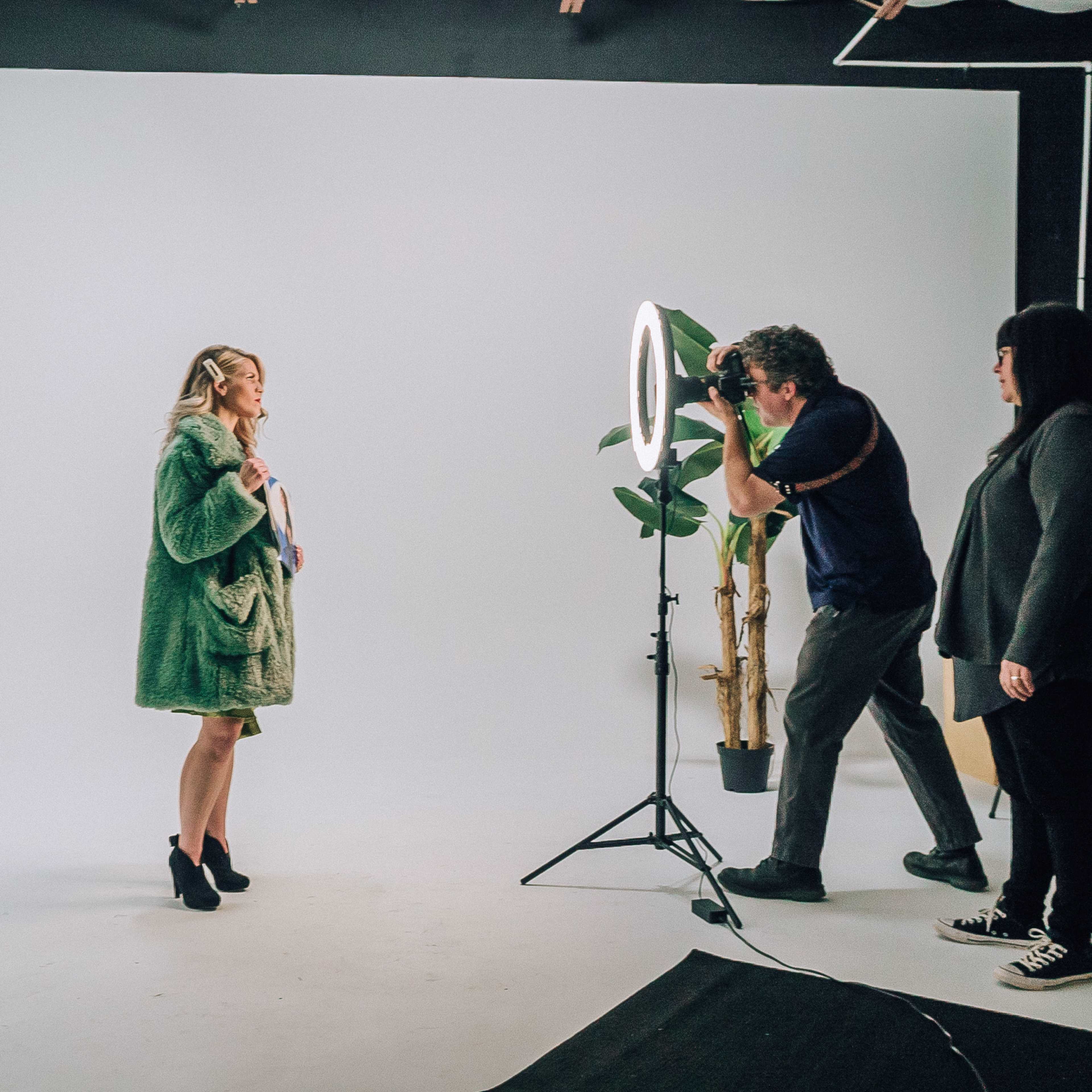 A photographer captures an image of a woman wearing a green coat in a studio setting, while another person observes.