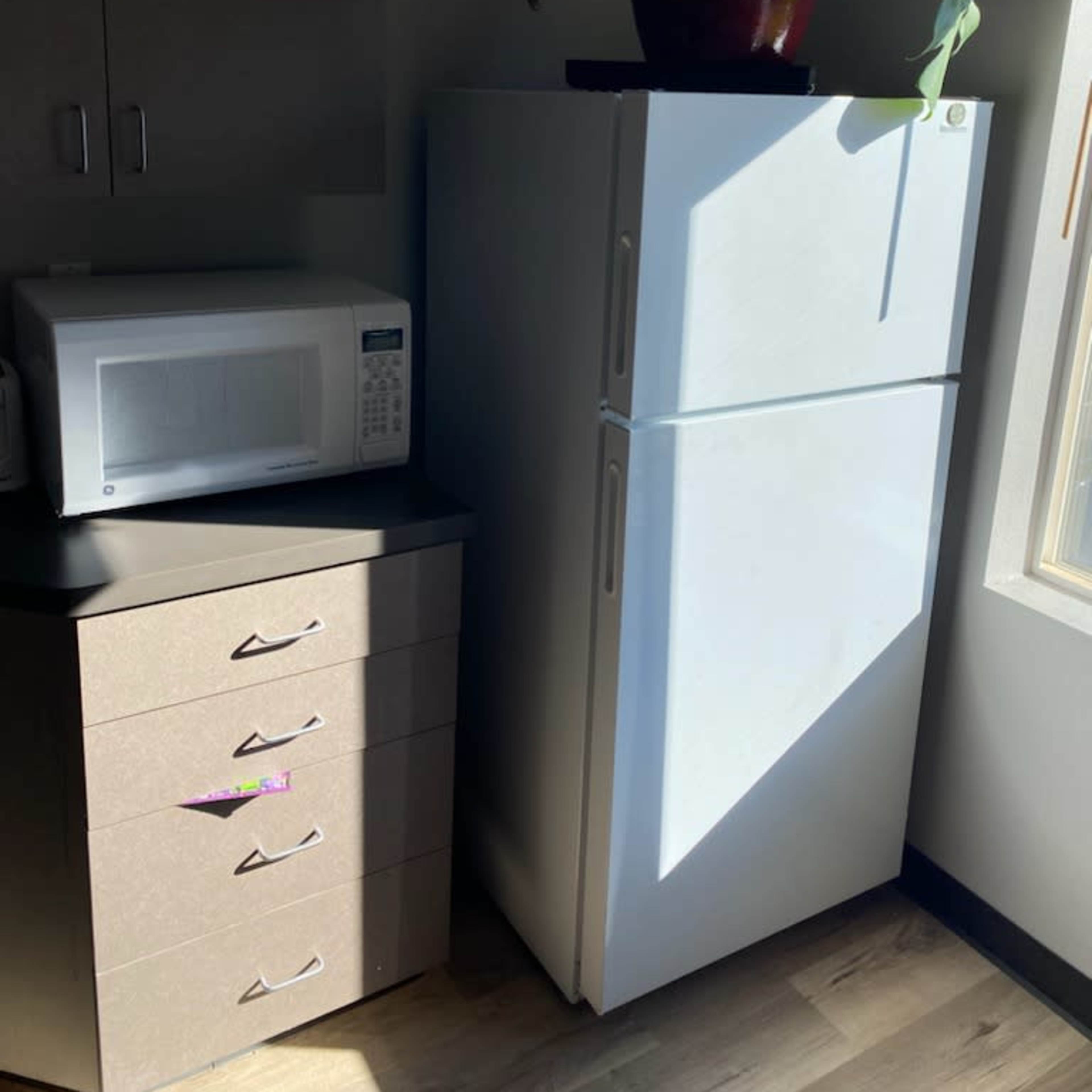 A white refrigerator next to a microwave and a set of drawers in a well-lit corner of a room.