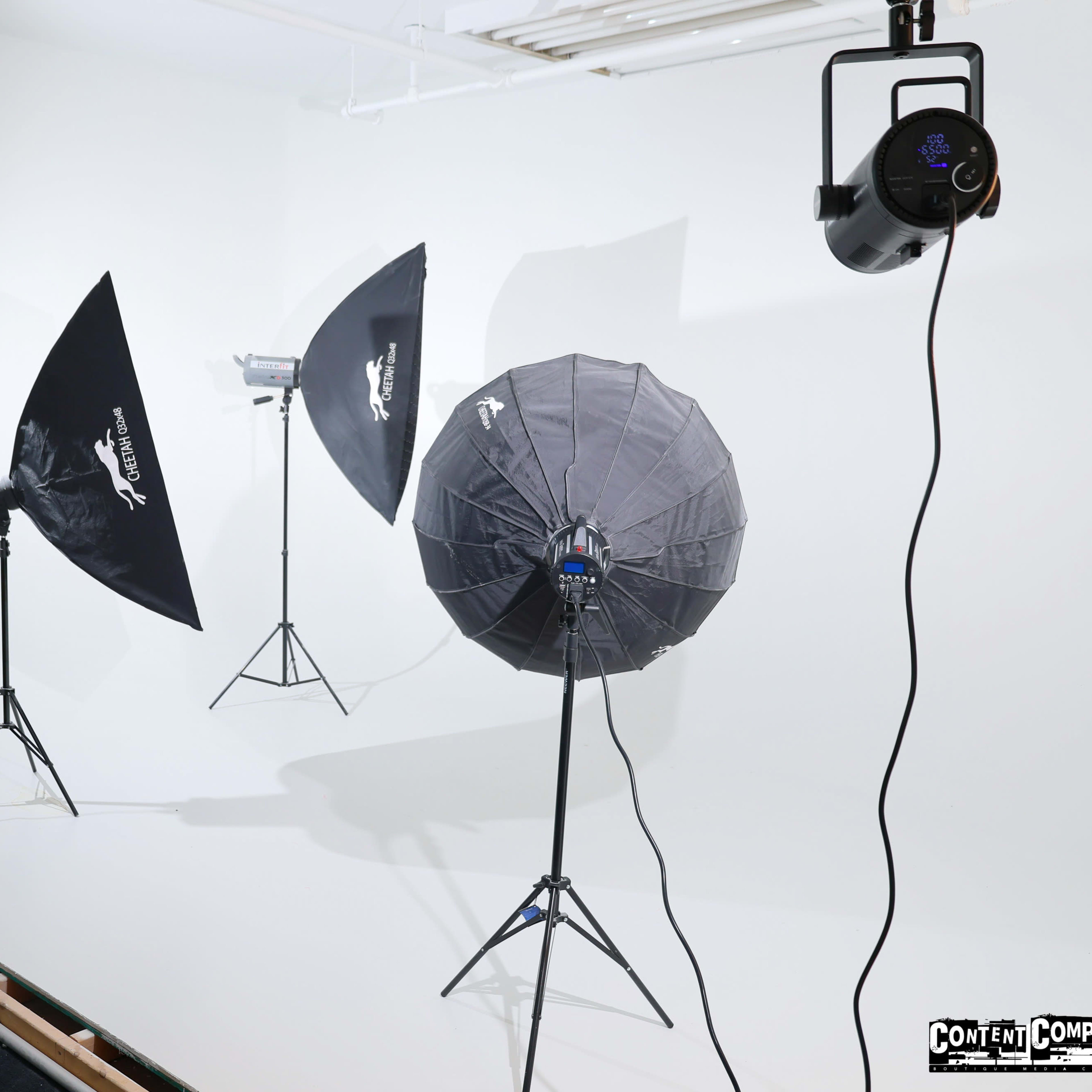 A photography studio setup with various softbox lights and an umbrella reflector on a white backdrop.