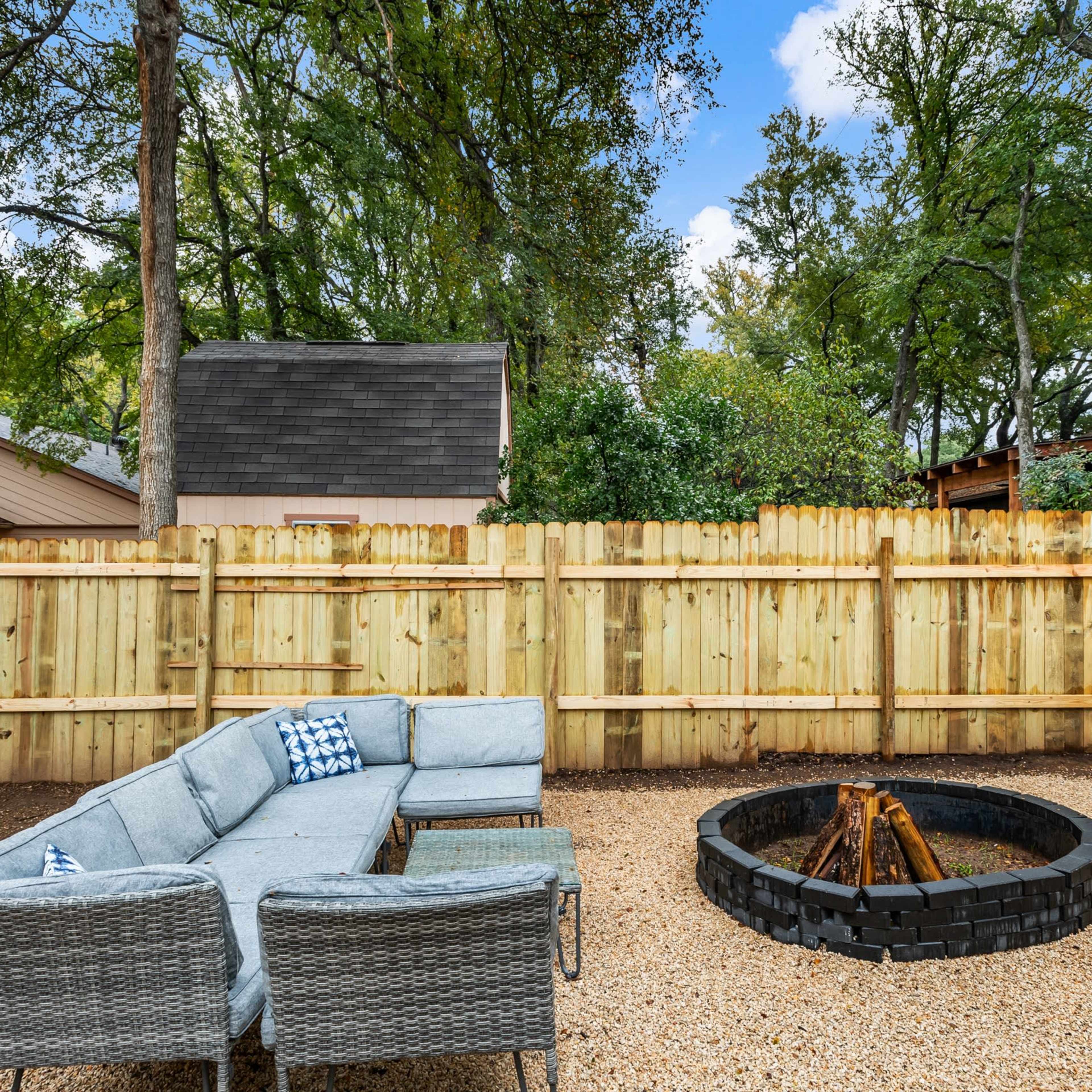 A fenced backyard featuring a circular fire pit surrounded by gravel and a sectional outdoor couch.