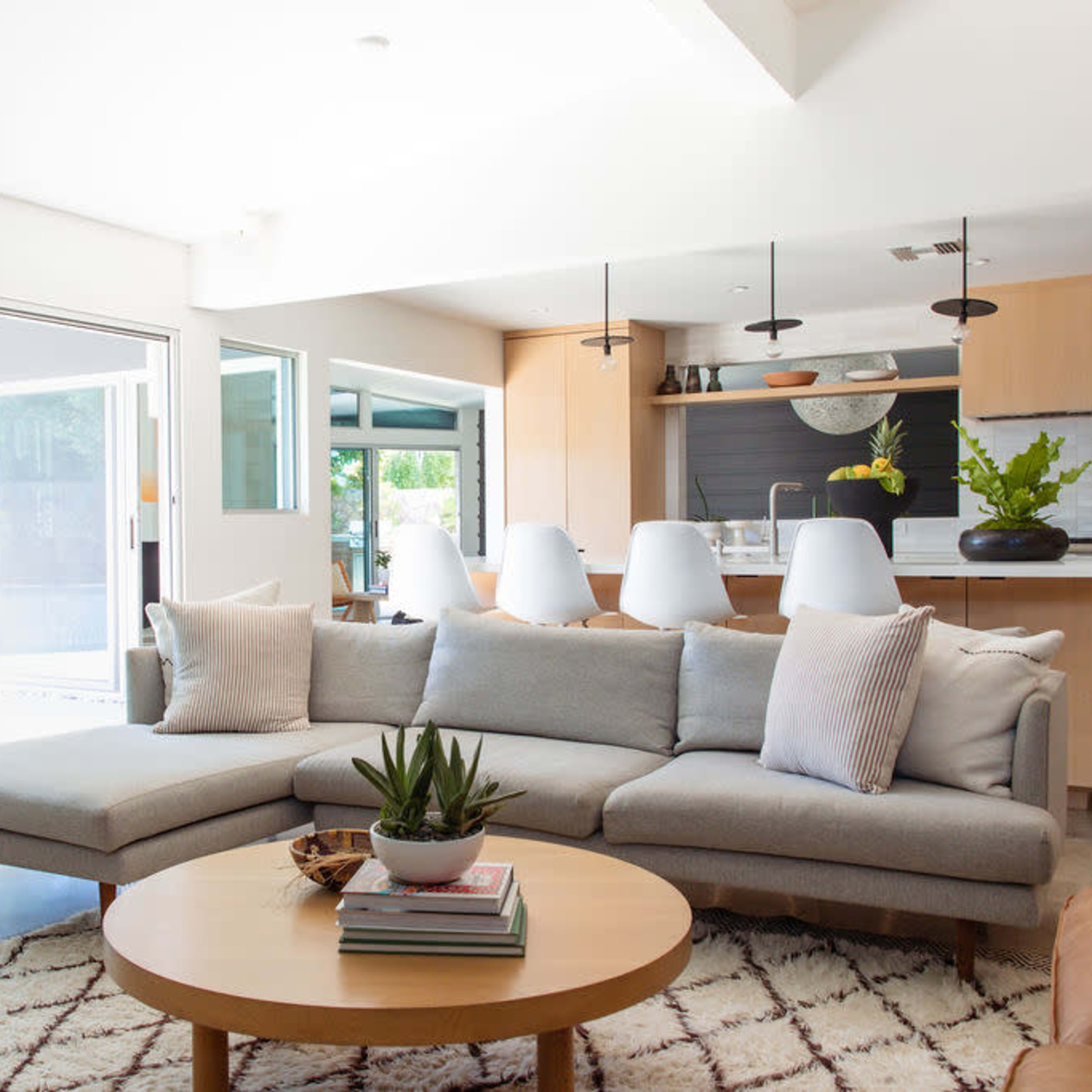 The living room features a gray sectional sofa, a round wooden coffee table, and large glass doors leading to an outdoor area with a swimming pool.