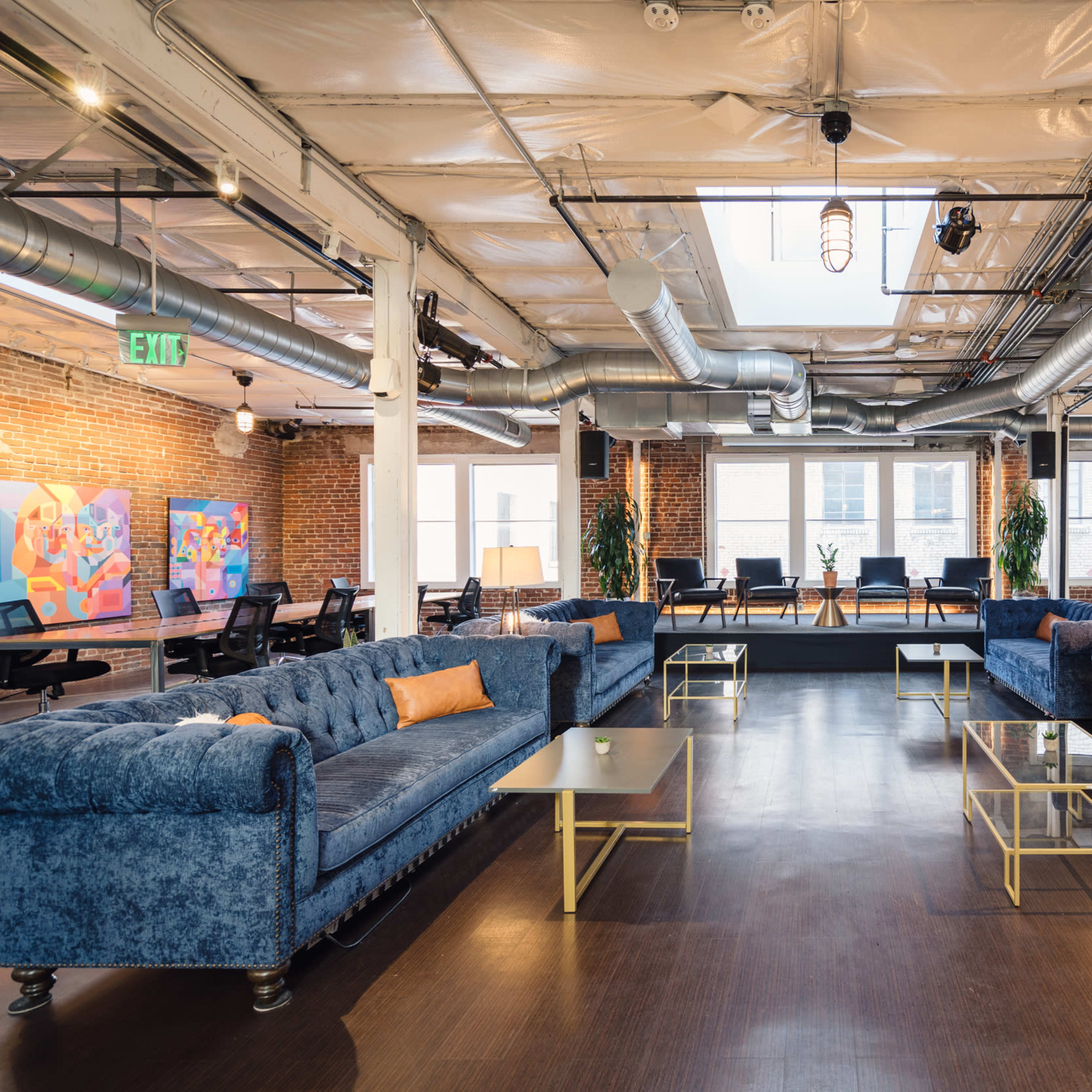 A spacious lounge area with two blue tufted sofas, glass coffee tables, and large windows letting in natural light.