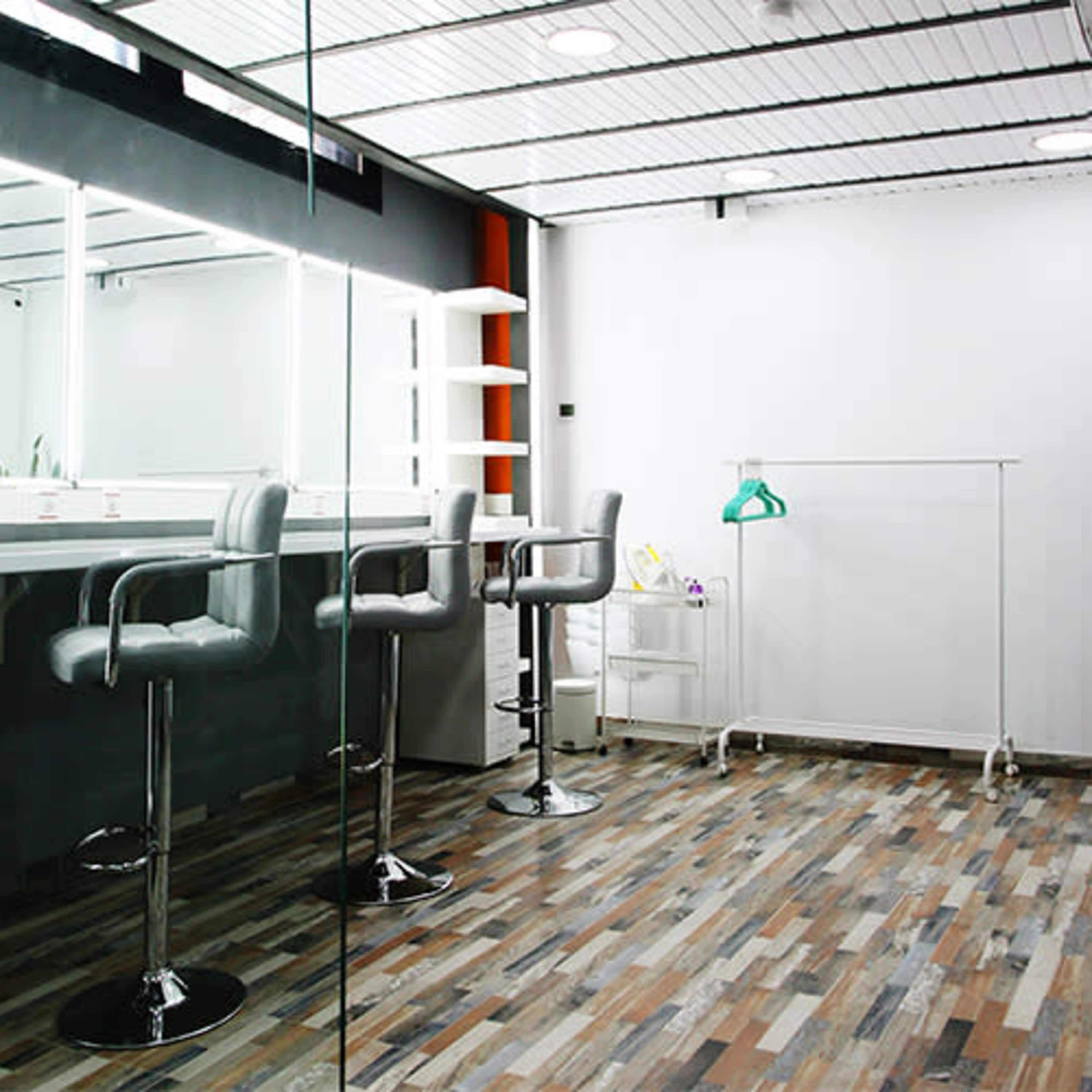 A modern dressing room with a mirrored wall, two barstools, and a clothing rack against a white background.
