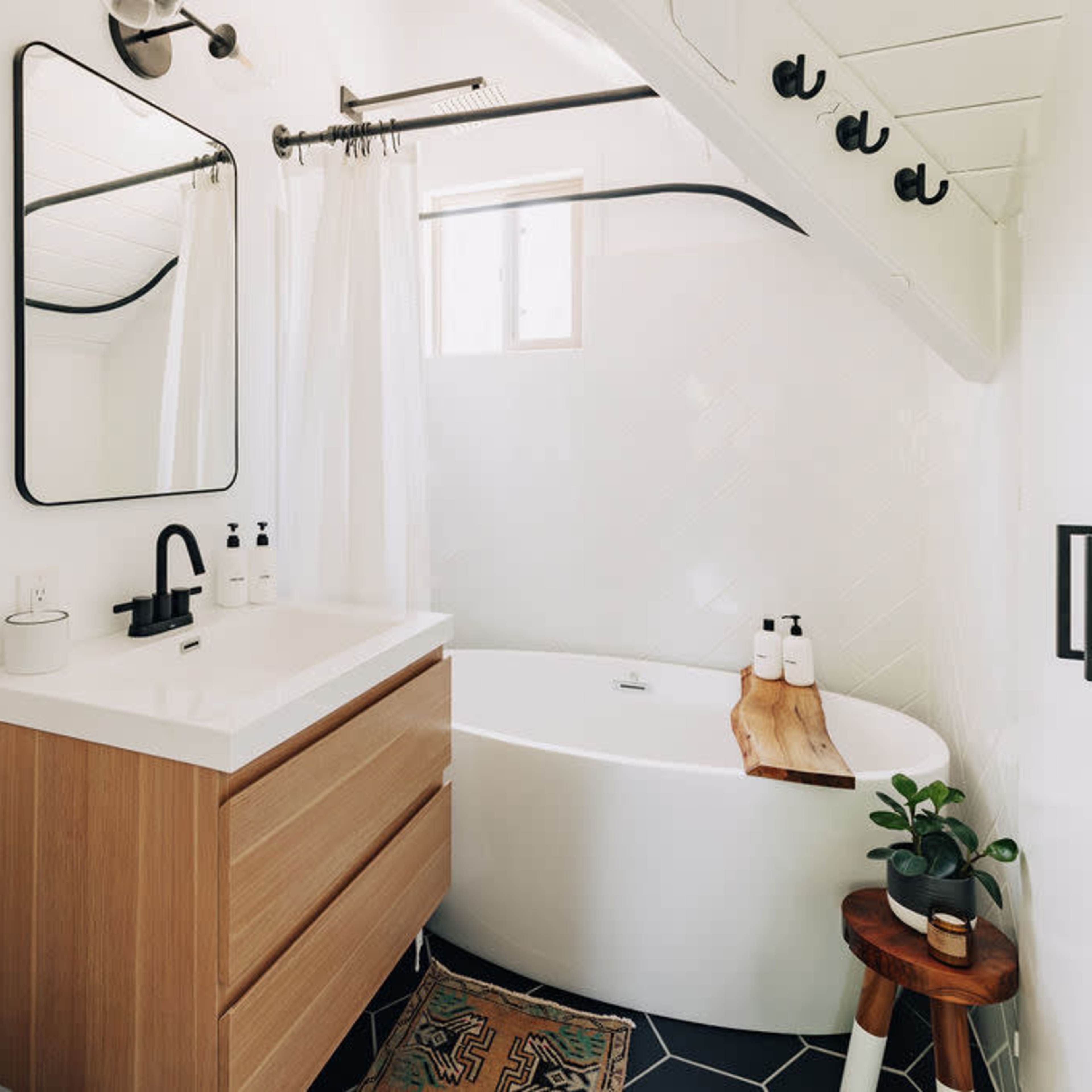 A modern bathroom featuring a freestanding tub, a wooden vanity with a sink, a large mirror, and minimalistic decor.