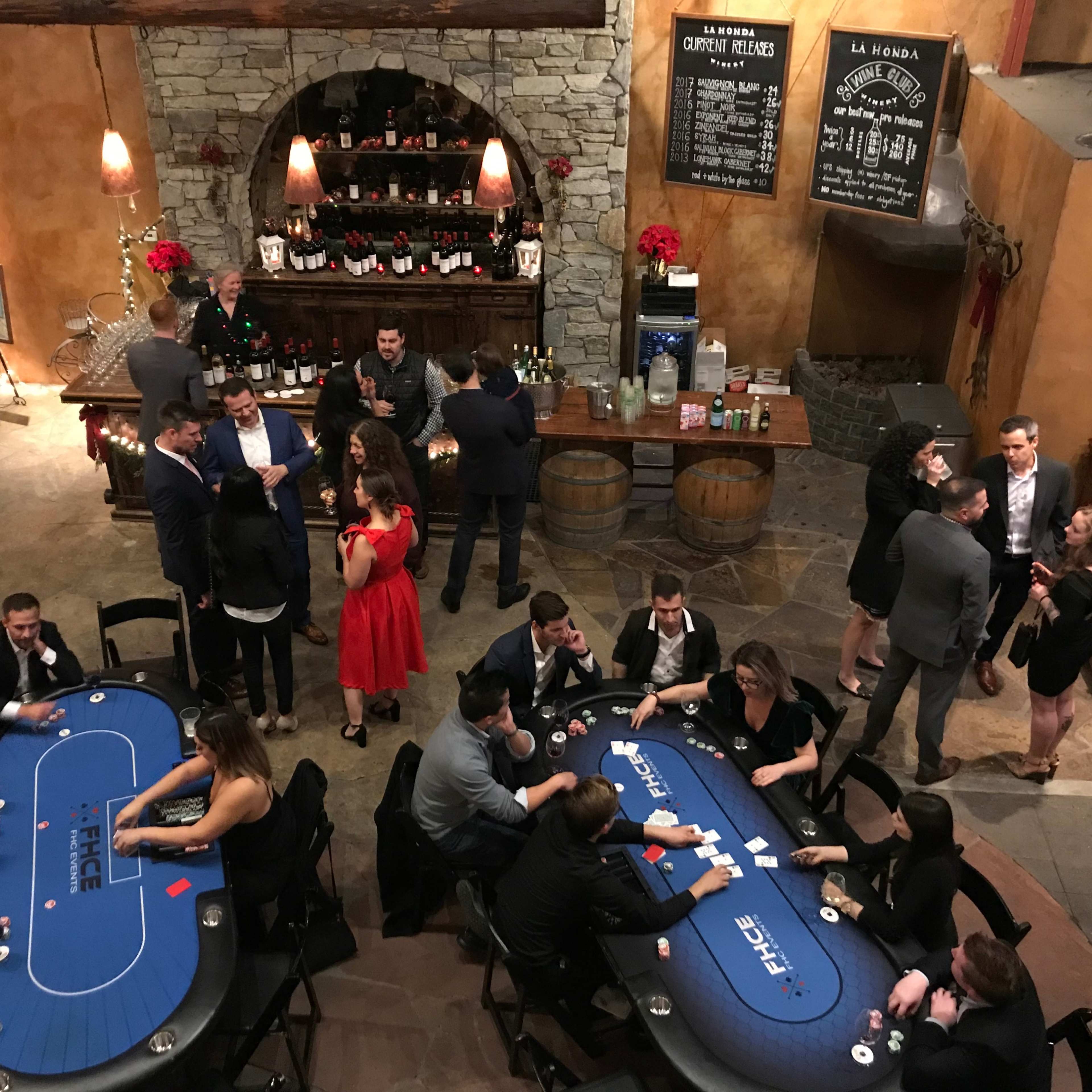 A group of people engages in conversation and gaming at tables in a warmly lit, rustic venue decorated for a festive occasion.