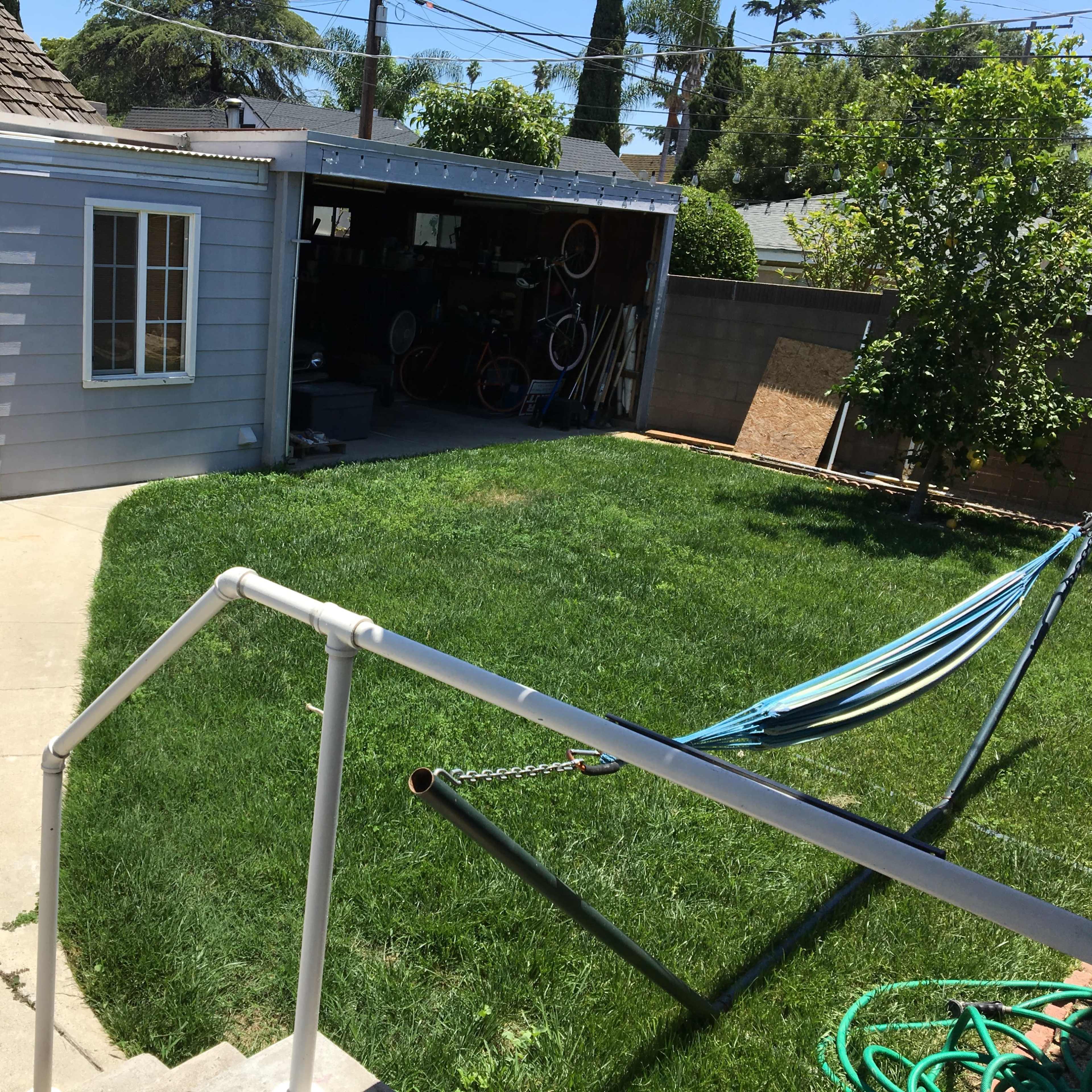 A backyard with a grassy area, a shed on the left, and a hammock set up on the right.