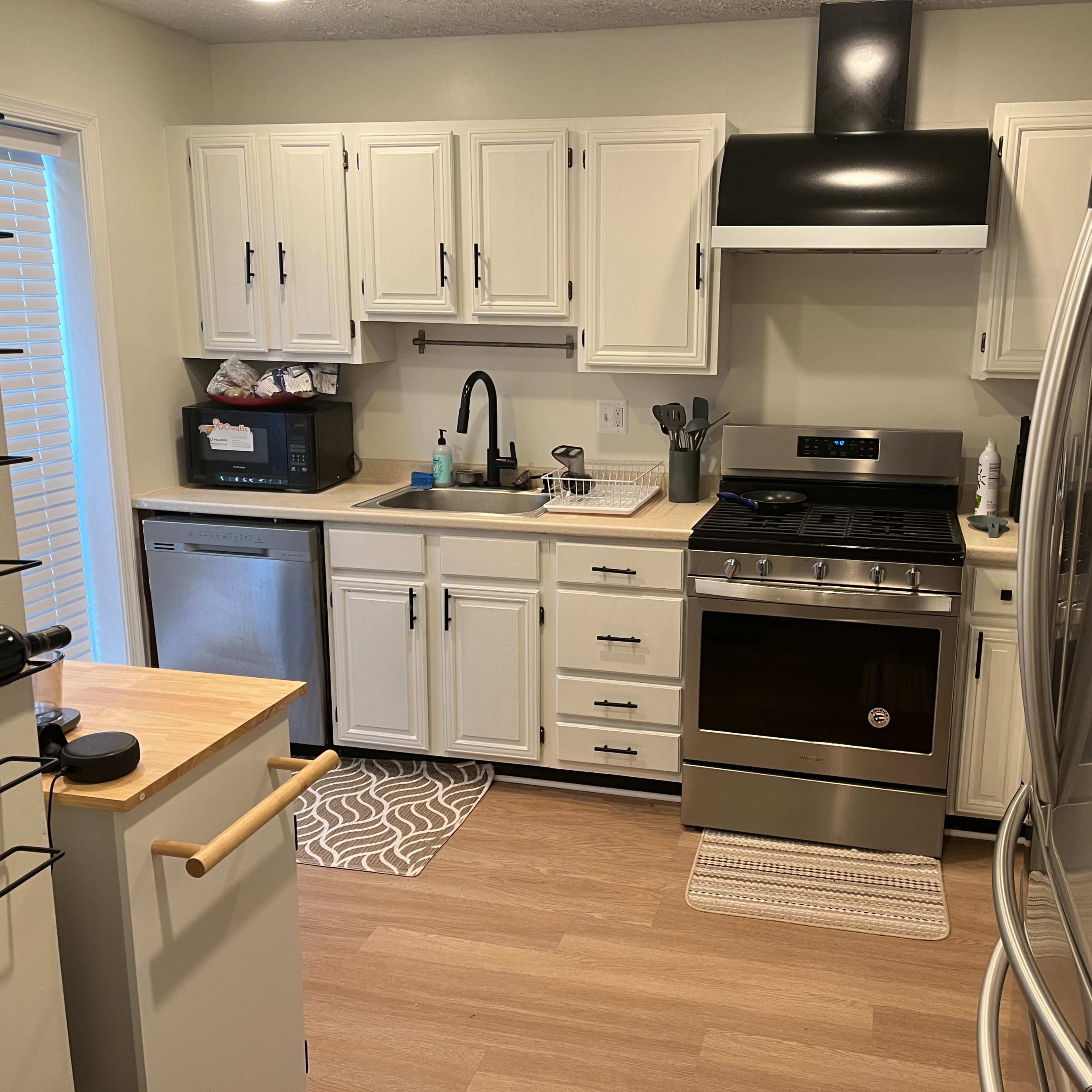 A modern kitchen features white cabinets, stainless steel appliances, and a light-colored wood floor.