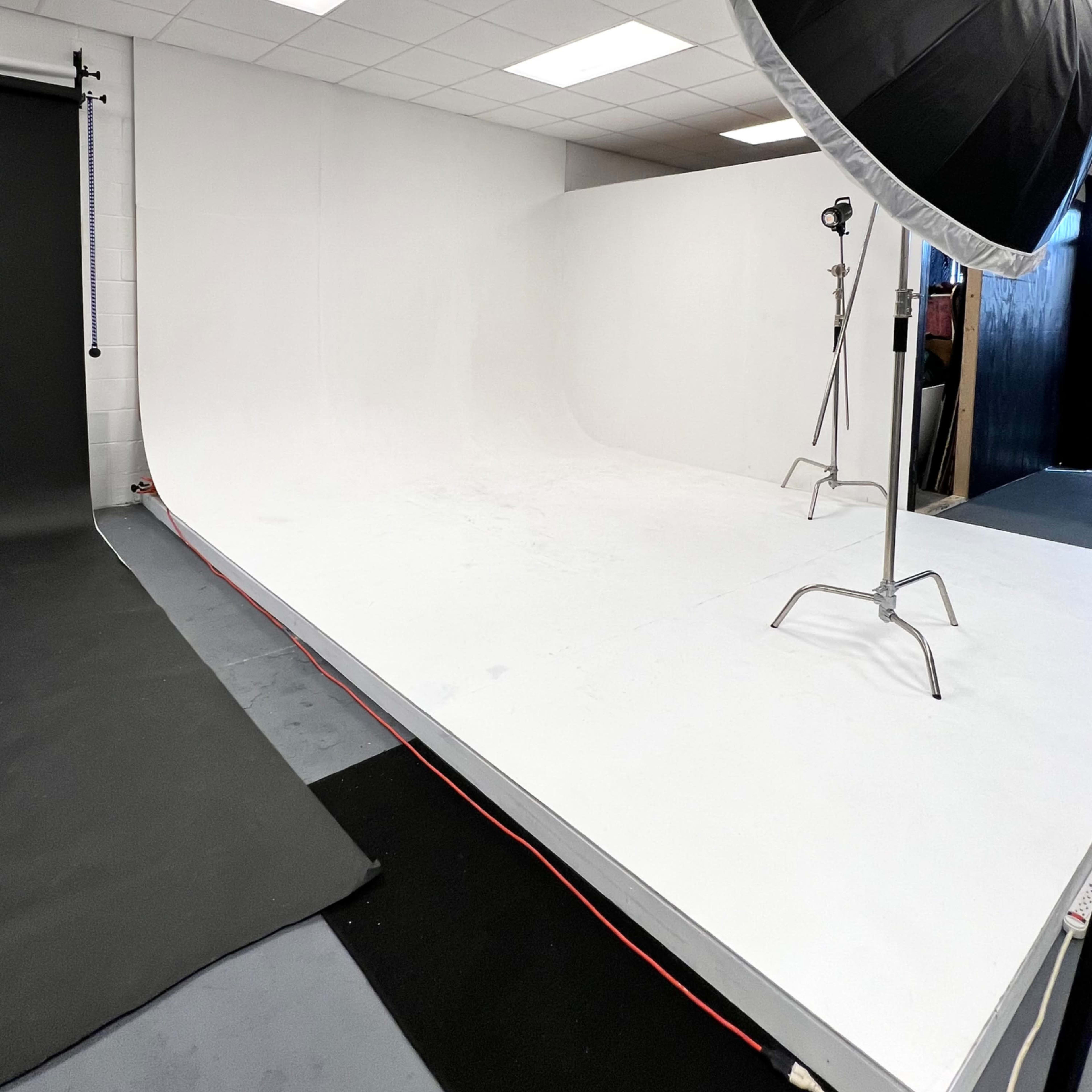 A photography studio with a white backdrop, softbox lighting, and a dark floor mat.