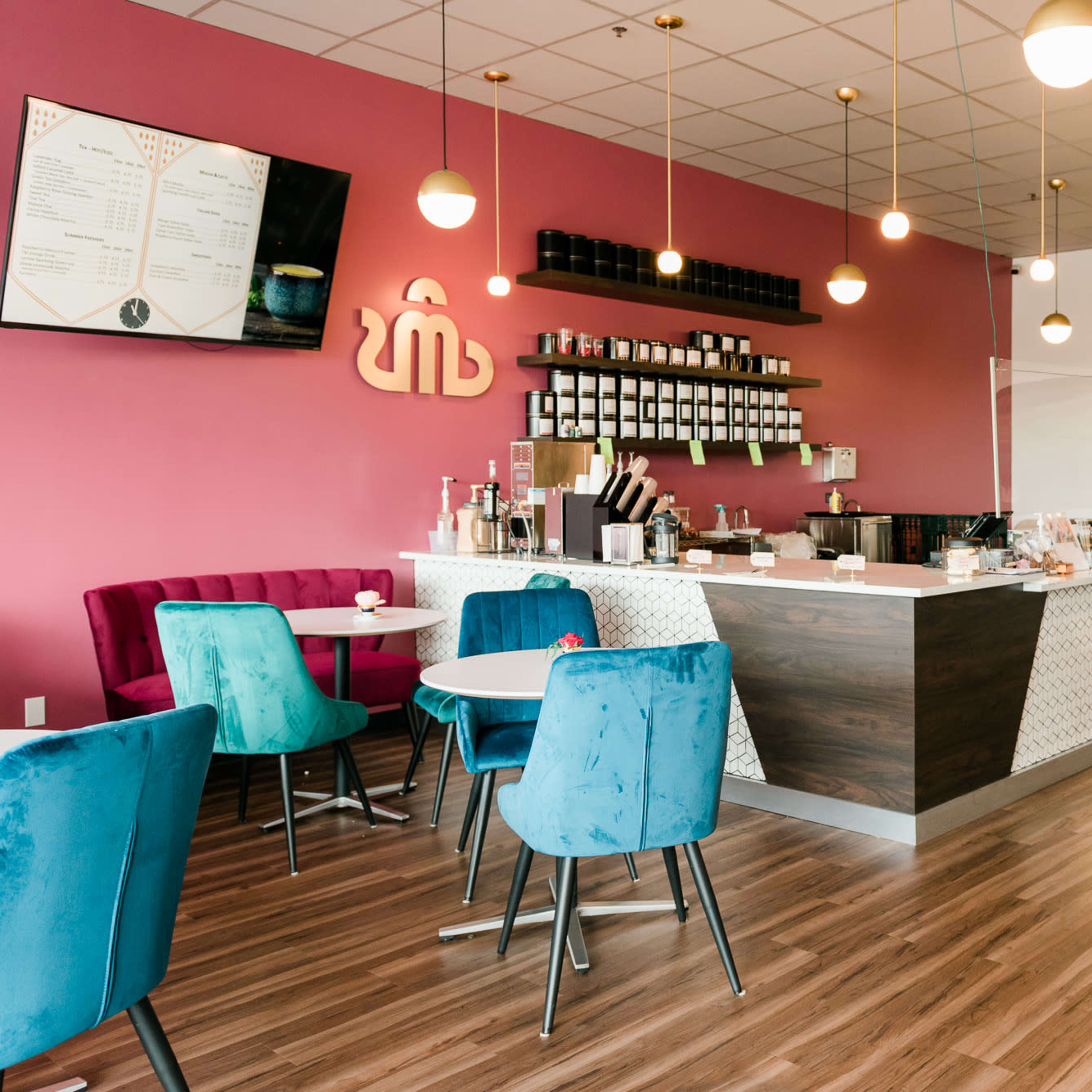 A cozy café interior with a pink wall, a service counter with a display case, and colorful seating arrangements.