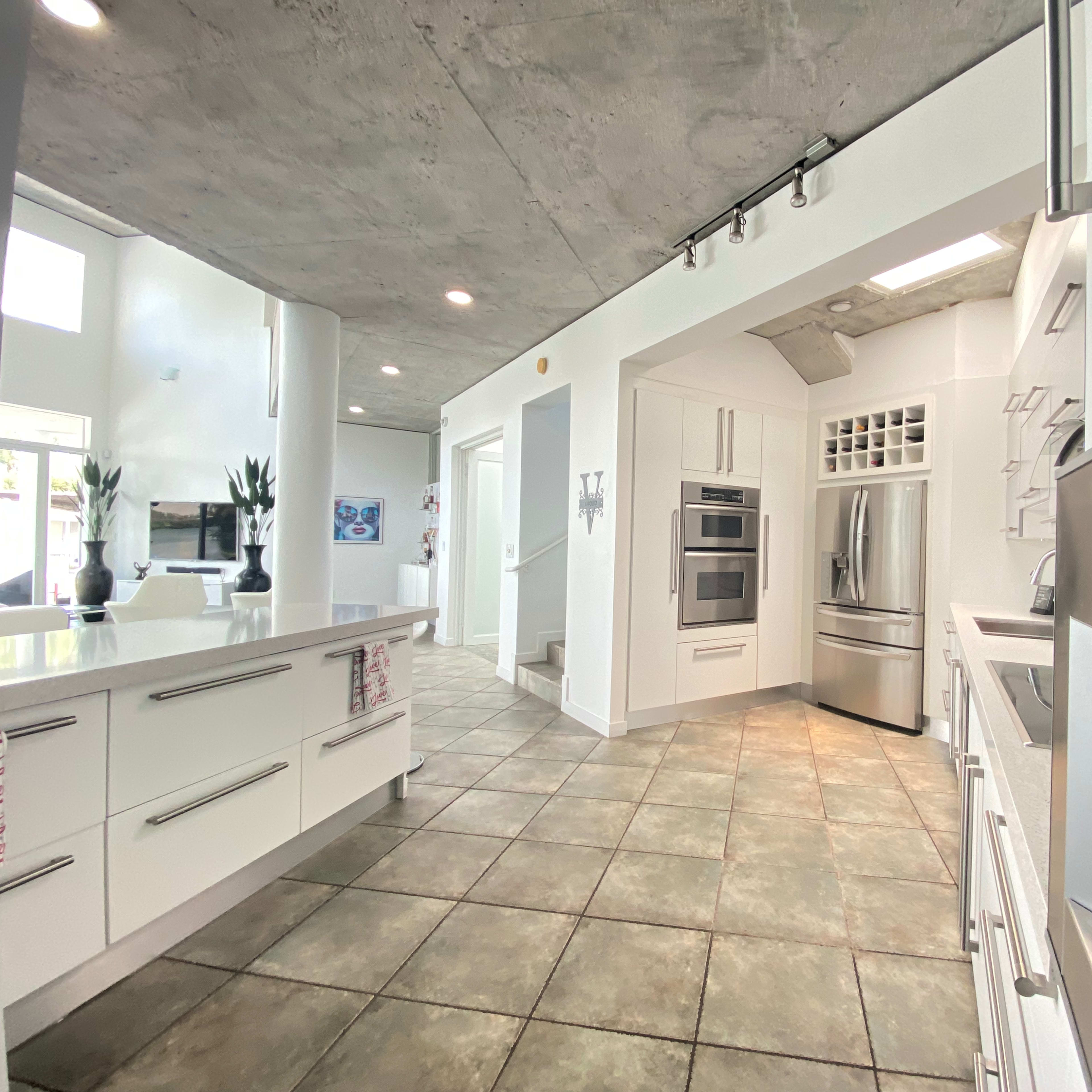 A modern kitchen featuring white cabinetry, a stainless steel refrigerator, and a spacious layout with gray tile flooring.