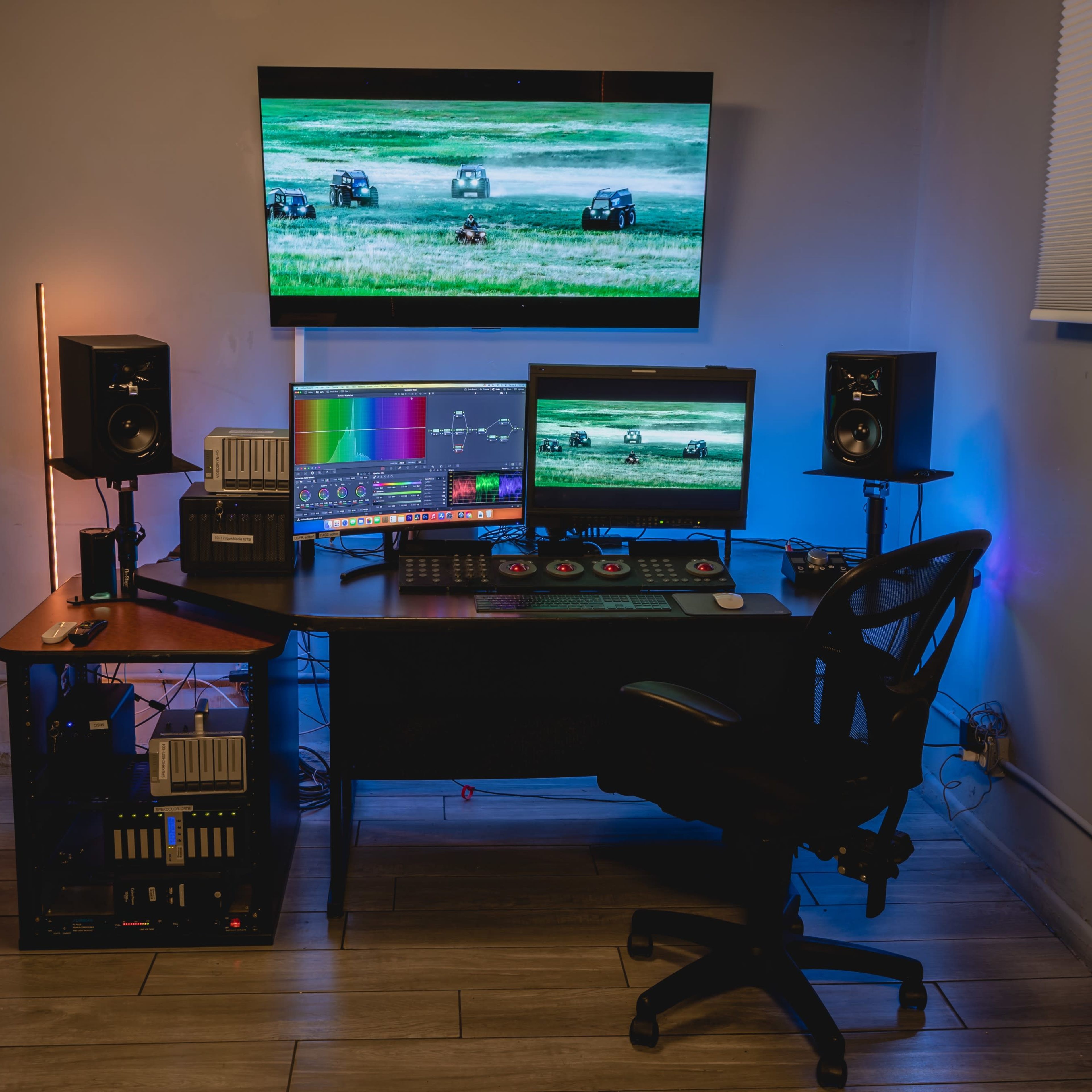 A modern computer workstation features multiple monitors, speakers, and colorful lighting, set against a neutral wall.