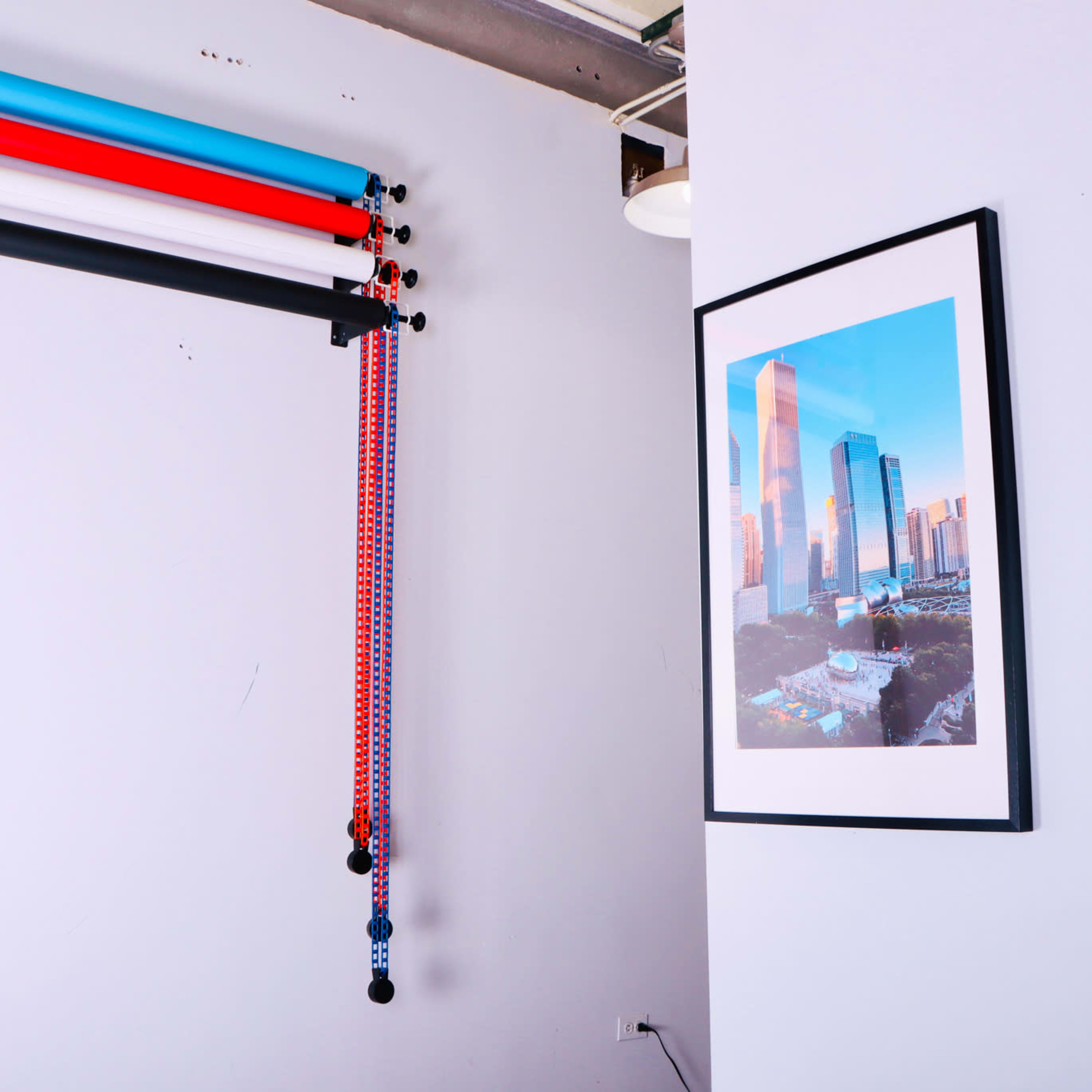 A corner of a room featuring colorful backdrop rolls mounted on the wall, two framed pictures, and a vinyl record on display.