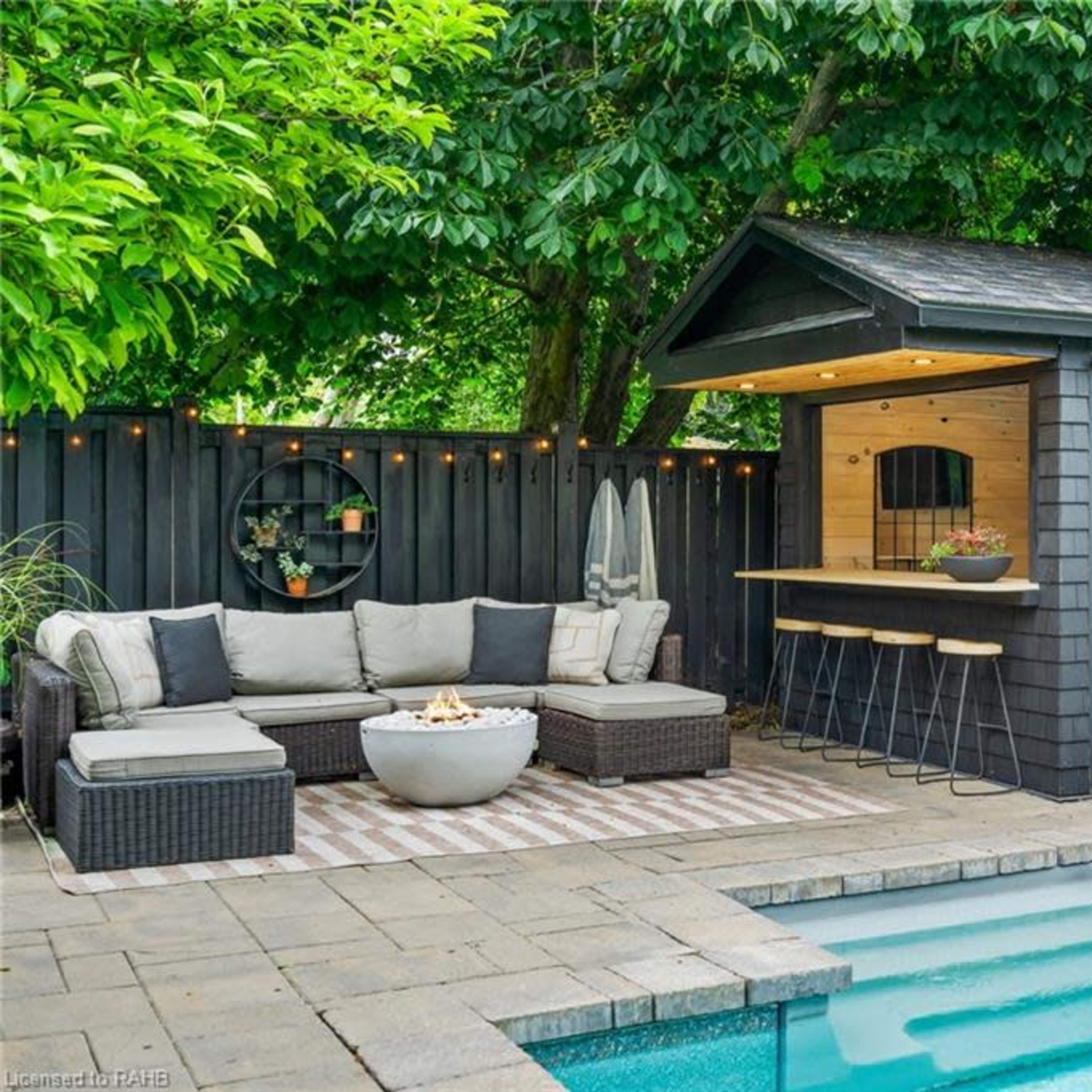 A backyard with a swimming pool, a cozy seating area with a fire pit, and a modern shed against a backdrop of greenery.