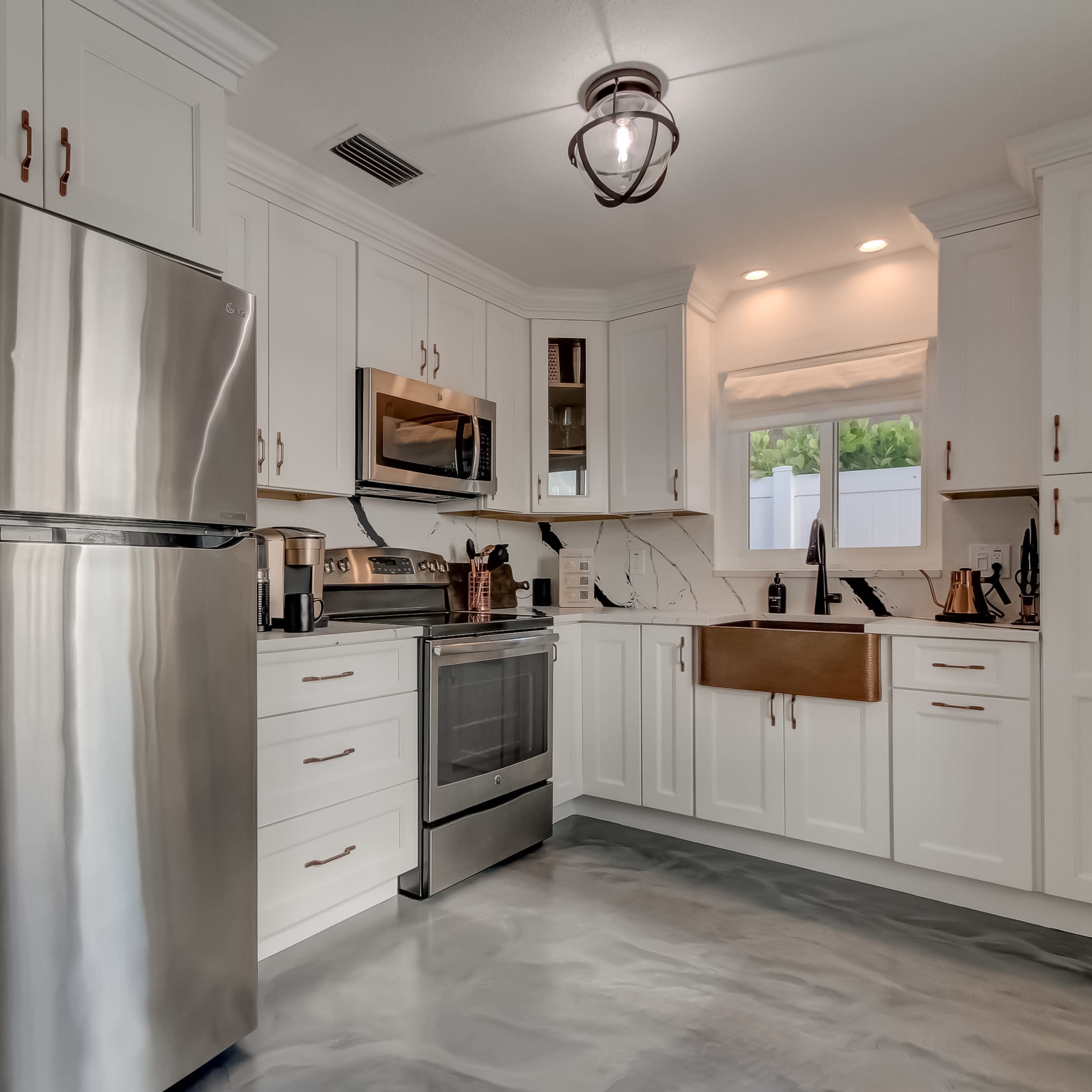 A modern kitchen features stainless steel appliances, white cabinetry, and a large sink beneath a window.