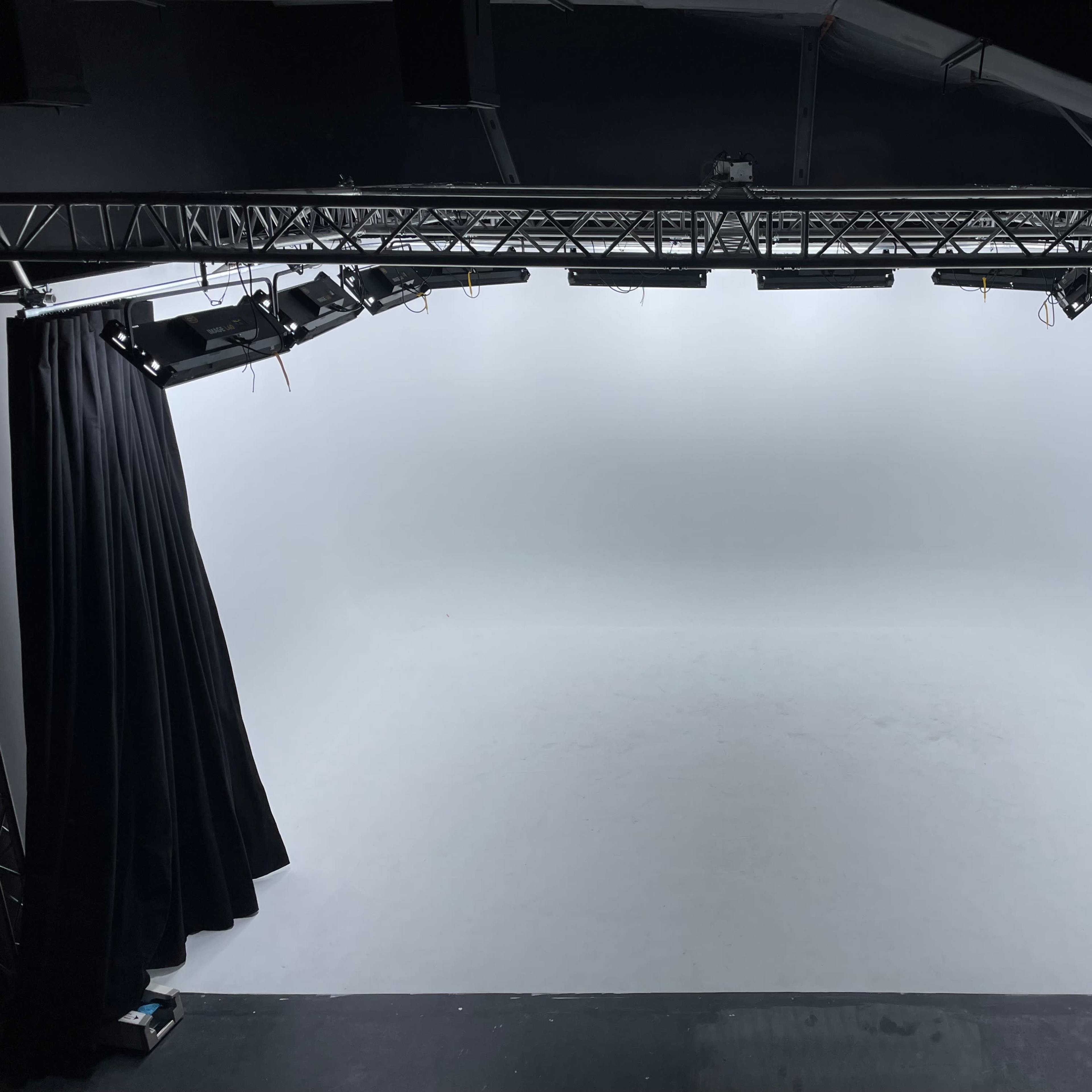 An empty stage with a white backdrop and black curtains on either side, illuminated by overhead lights.