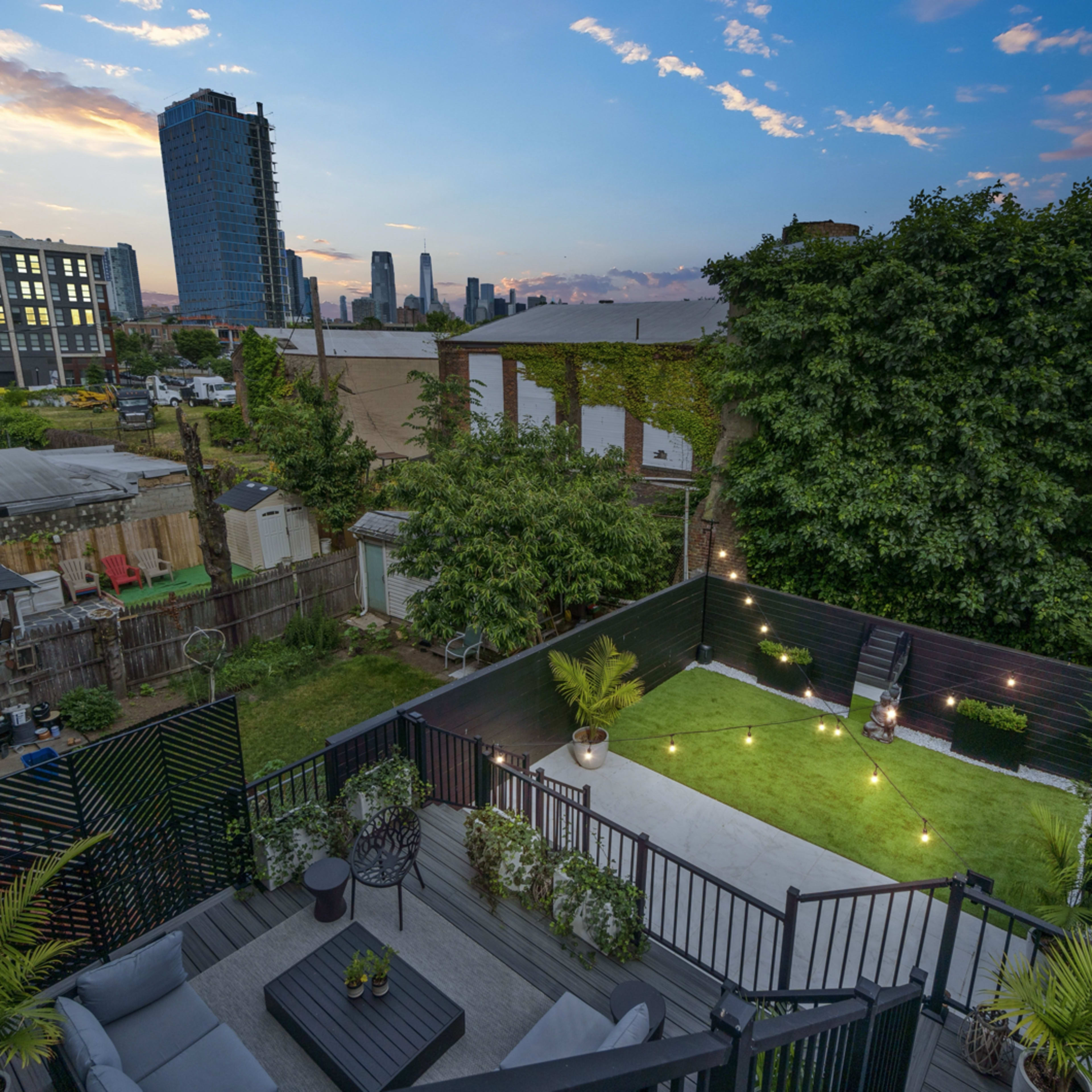 A rooftop garden with green grass, seating, and plants, overlooking a city skyline at dusk.