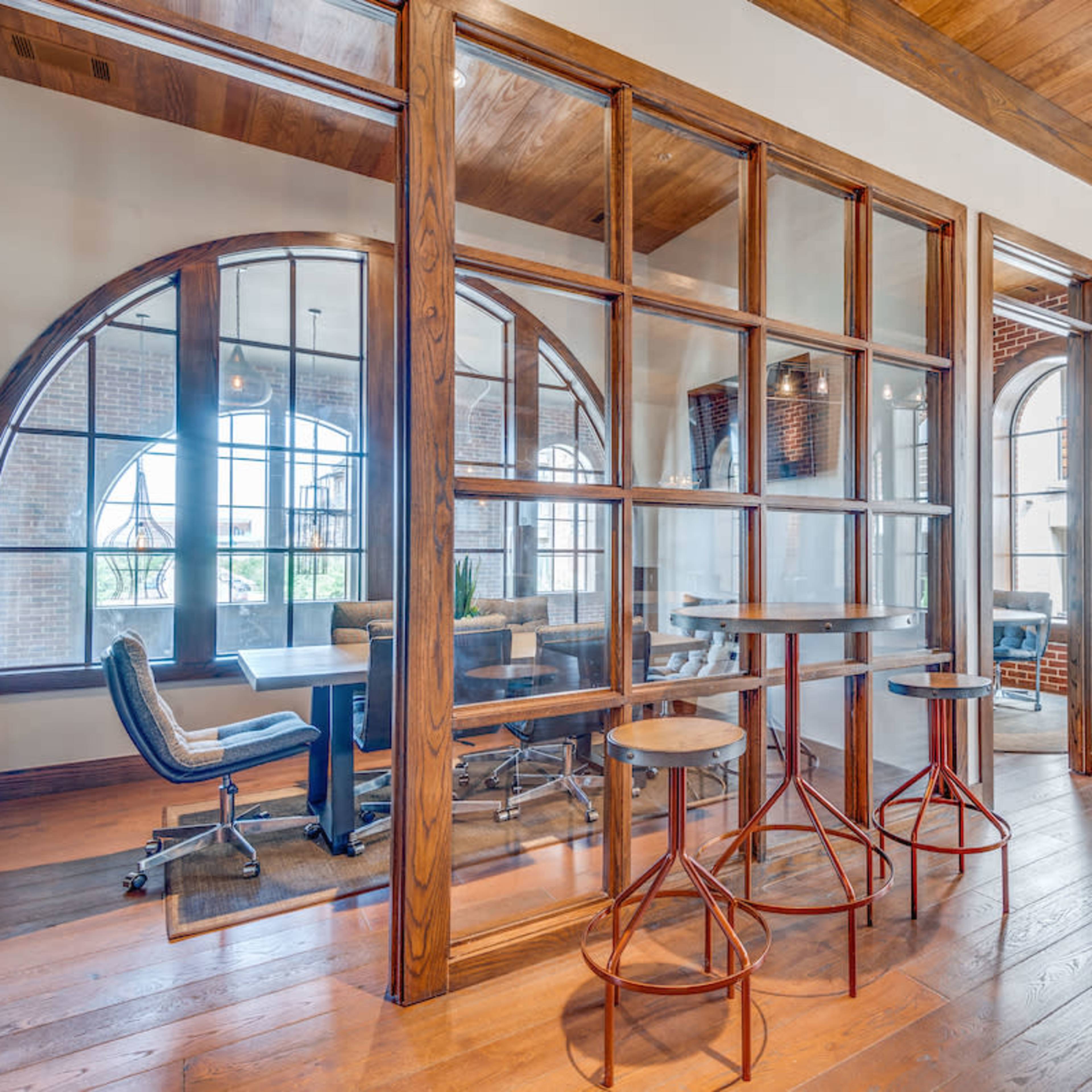 A modern office space featuring wooden floors, glass partitions, and a seating area with a purple upholstered chair.