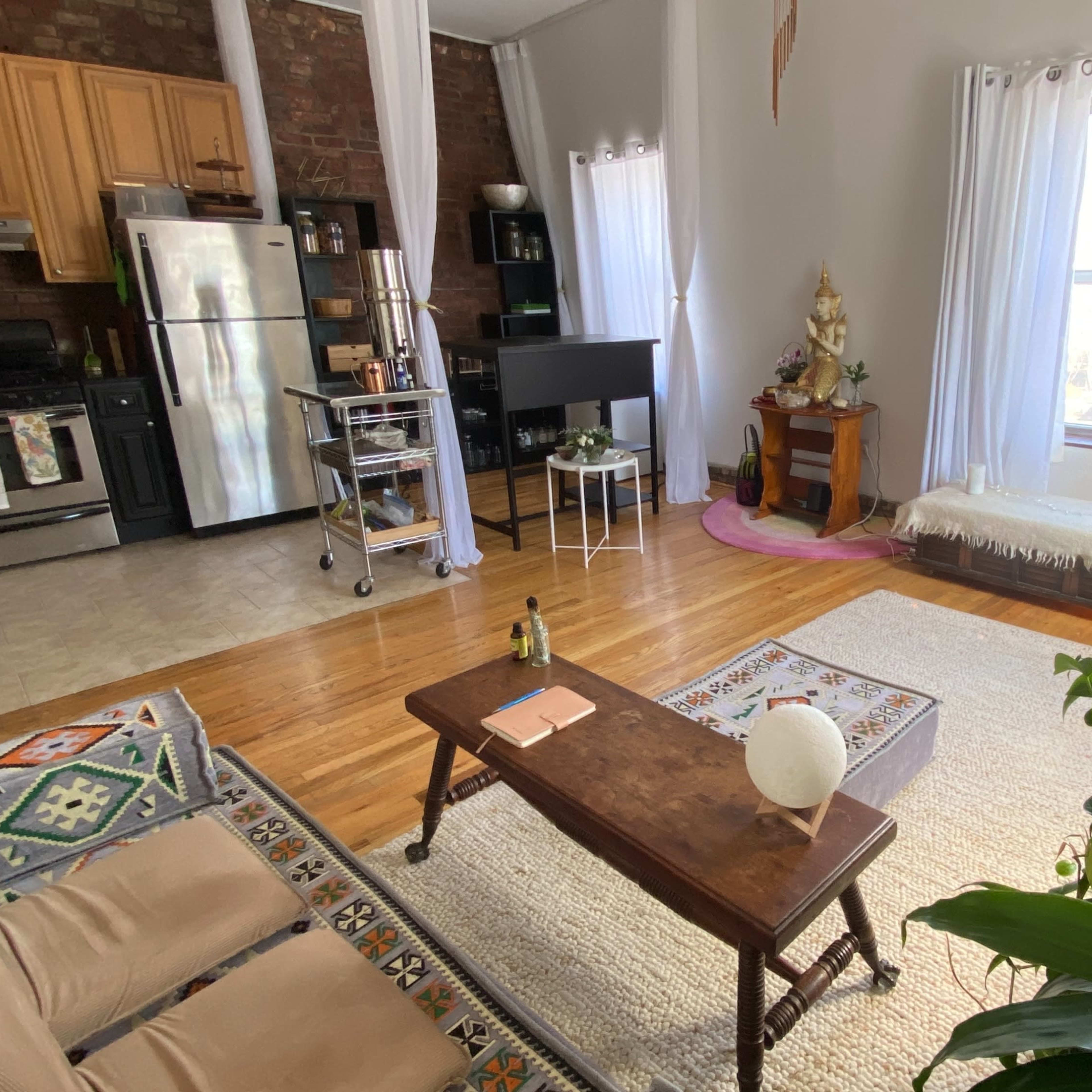 A living room with wooden floors, a sofa, a coffee table, a small dining area, and several potted plants.