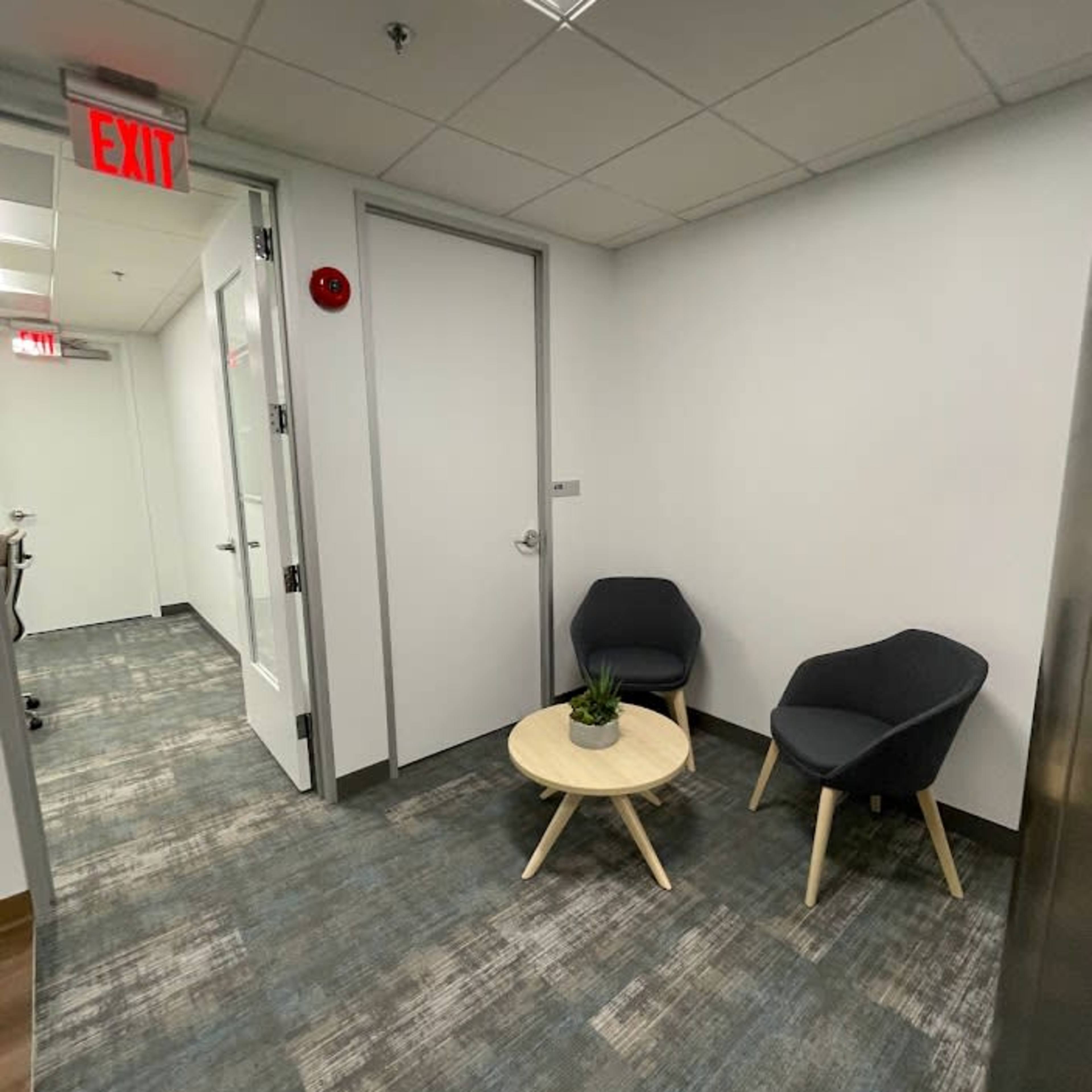 A conference room features a long wooden table surrounded by six beige chairs, with a television mounted on a blue wall and a landscape print hanging nearby.