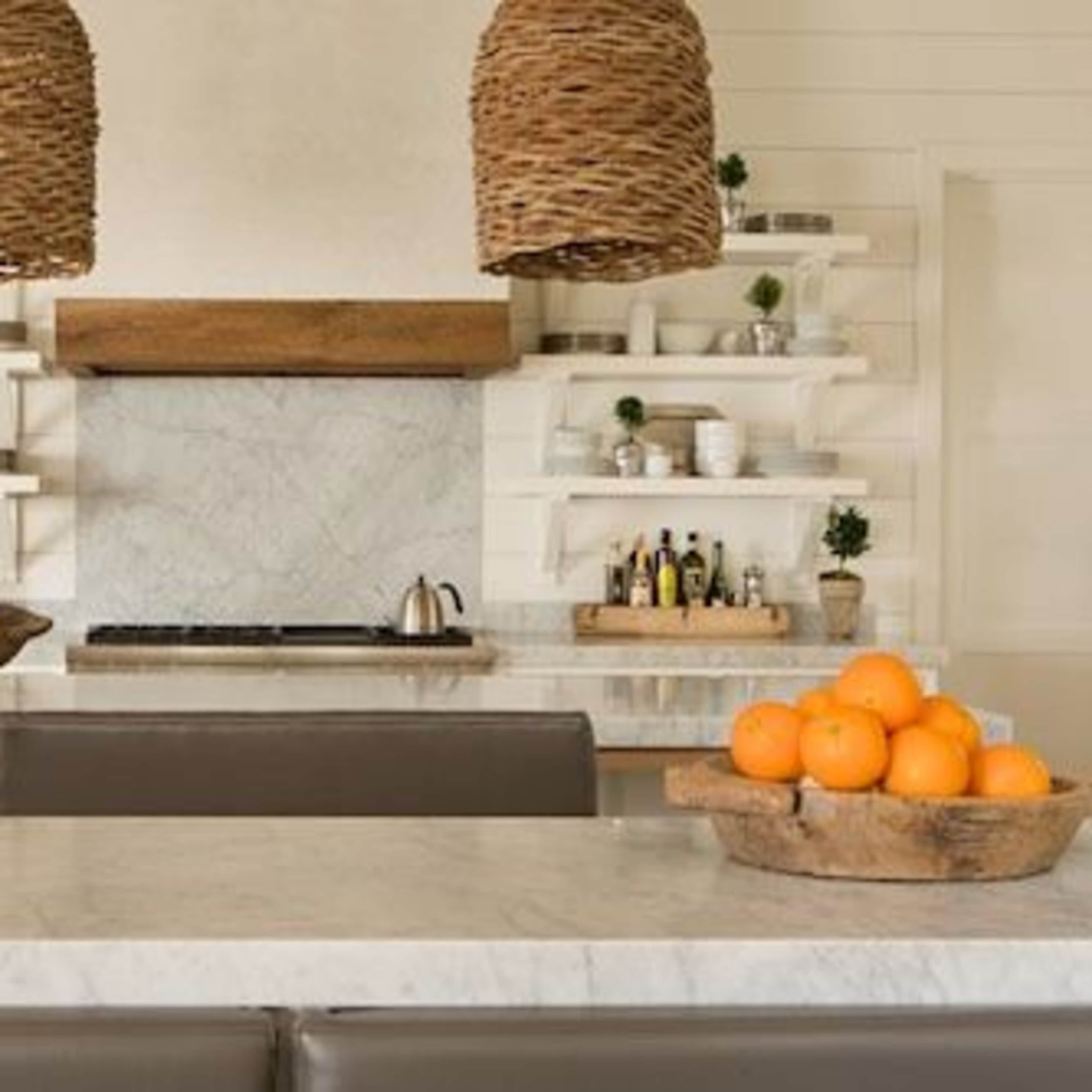 A modern kitchen features a marble countertop, open shelves with tableware, and two woven pendant lights hanging above.