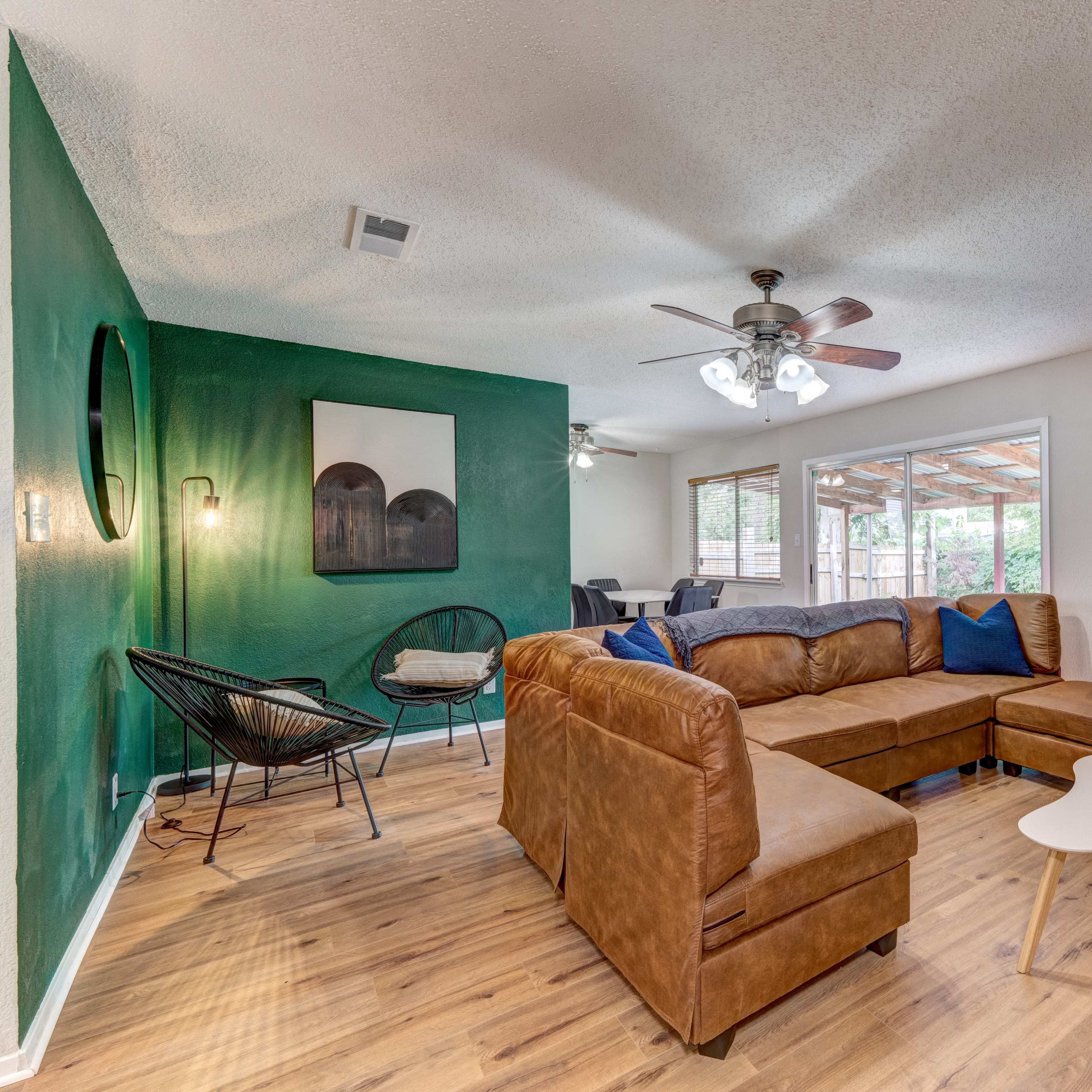A living room featuring a sectional sofa, a small coffee table, and a ceiling fan, with green and beige walls and large windows allowing natural light in.
