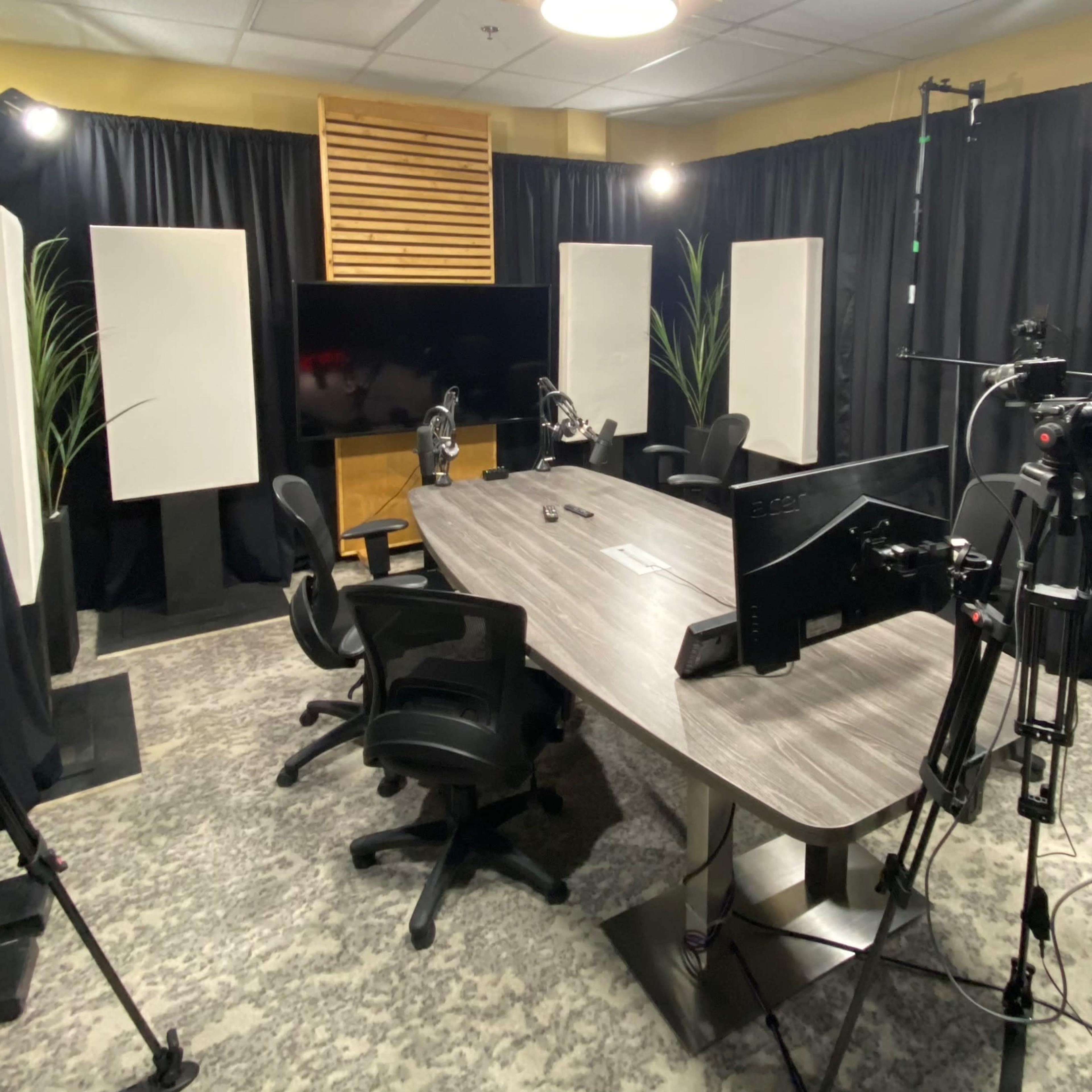 A recording studio equipped with multiple cameras, a large table with chairs, and sound absorption panels.