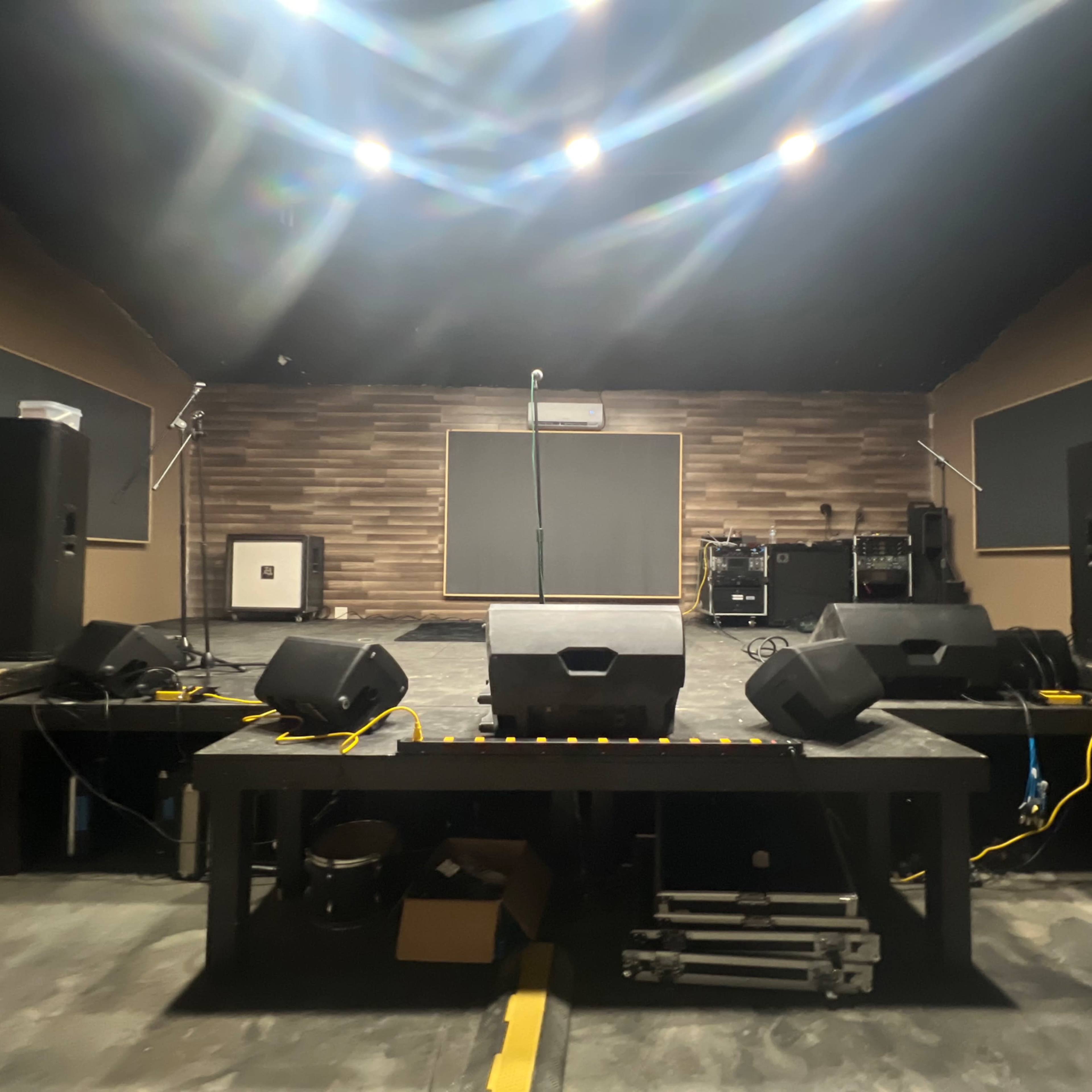 A performance stage with speakers, a microphone stand, and audio equipment in a dimly lit room.