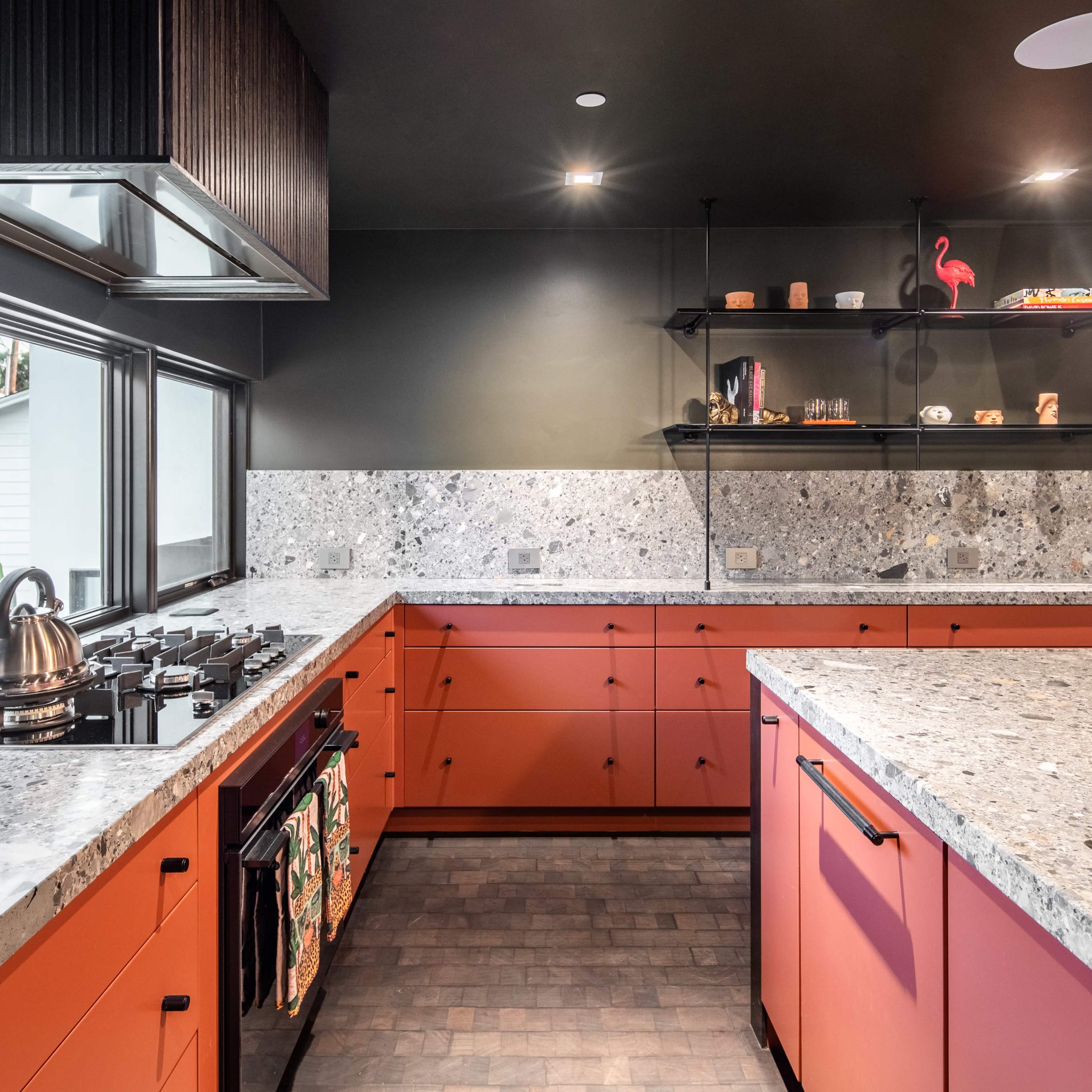 A modern kitchen with orange cabinets, a gray countertop, and stainless steel appliances.