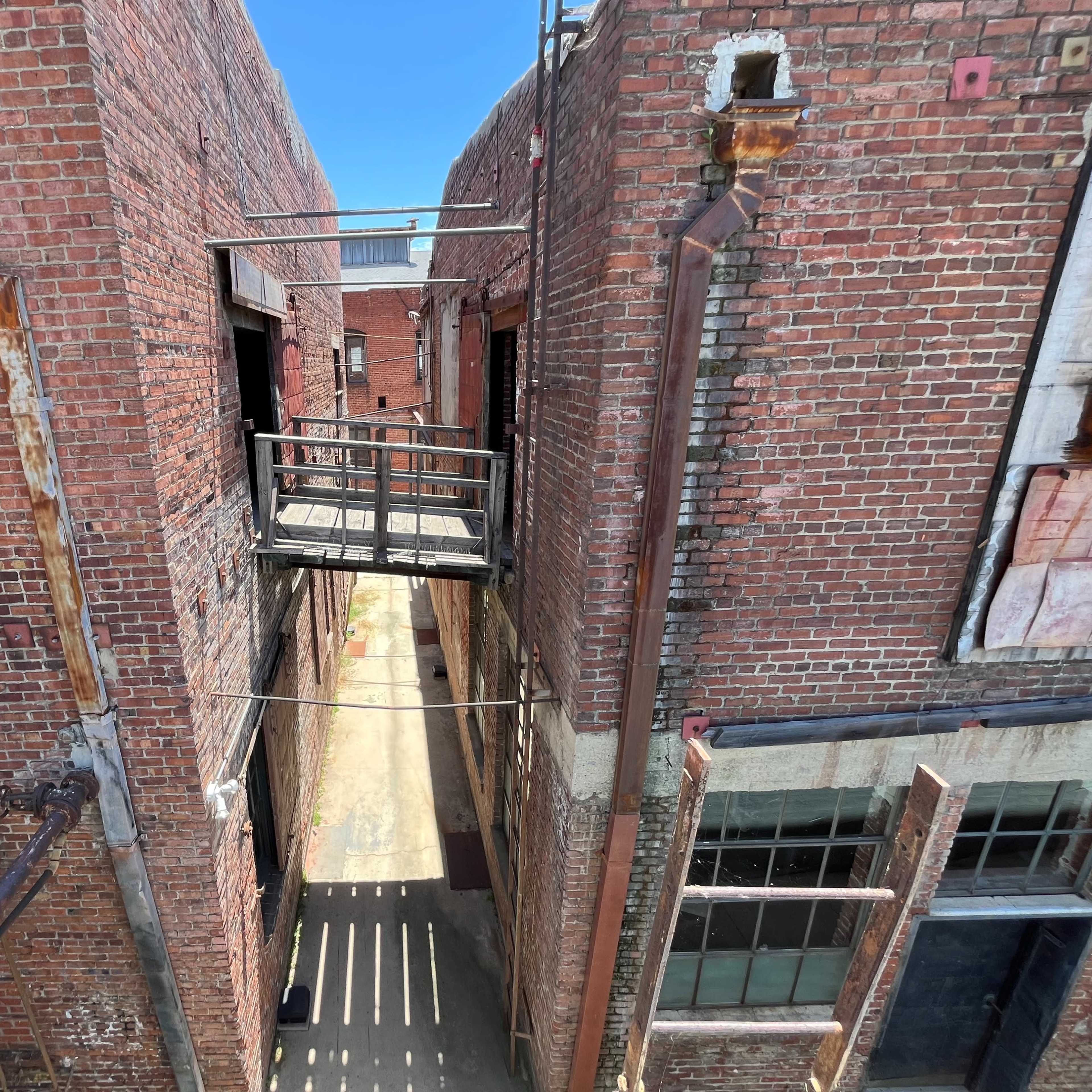 A narrow passage between two brick buildings with exposed metal walkways and an open sky above.