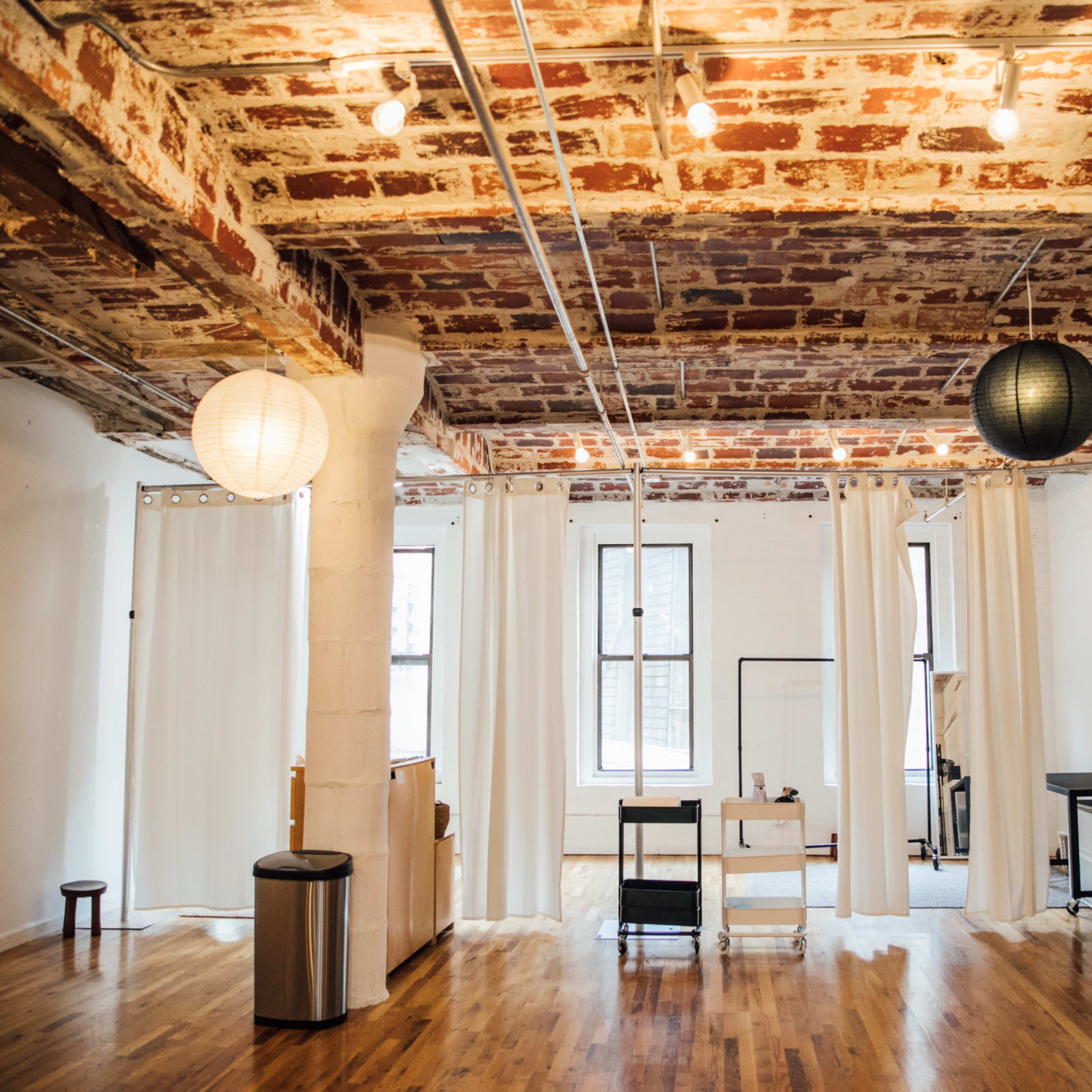 A spacious, minimalistic room with brick ceilings, wooden floors, and soft lighting from pendant lamps.