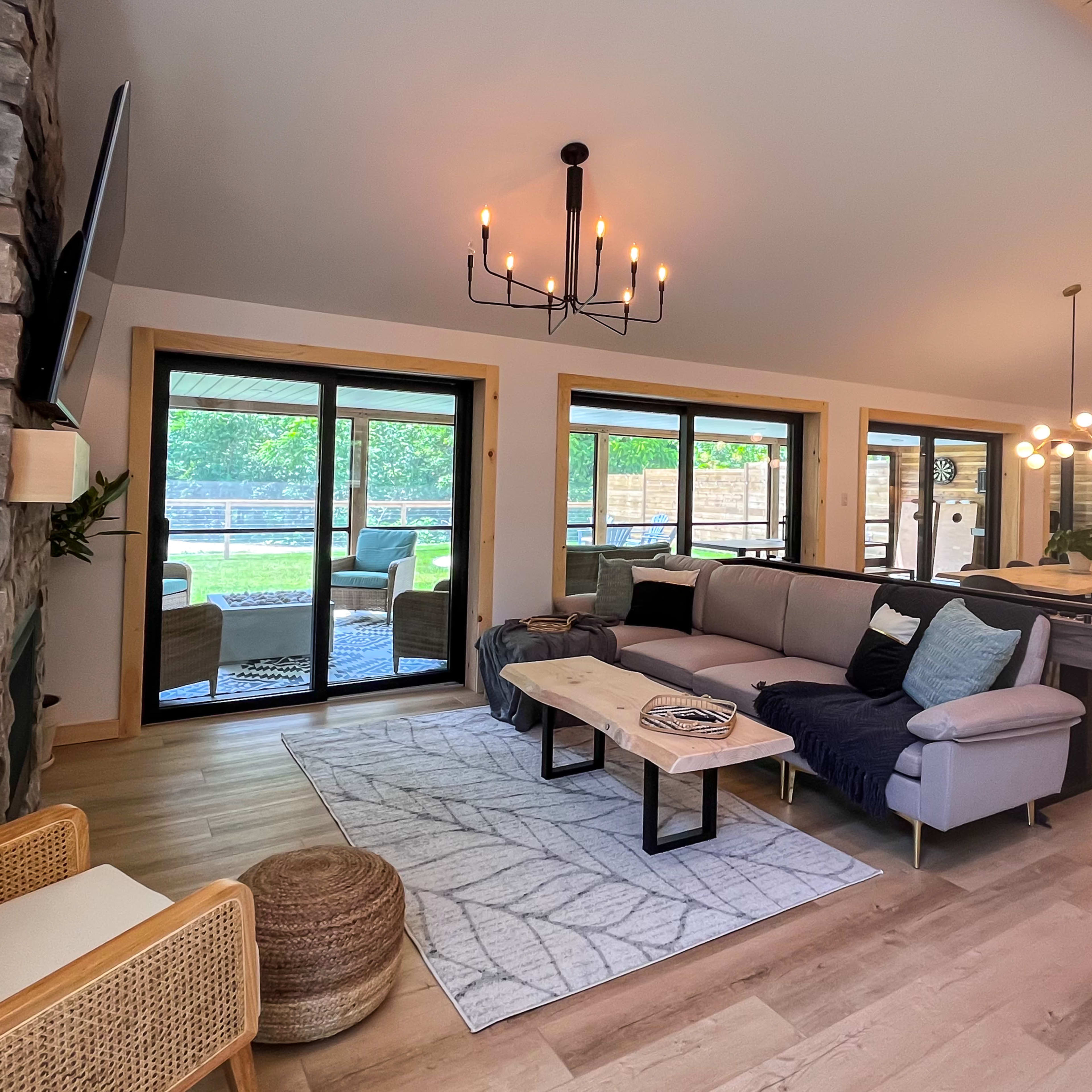 A modern living room featuring a sectional sofa, a wooden coffee table, and large glass doors opening to a green outdoor space.