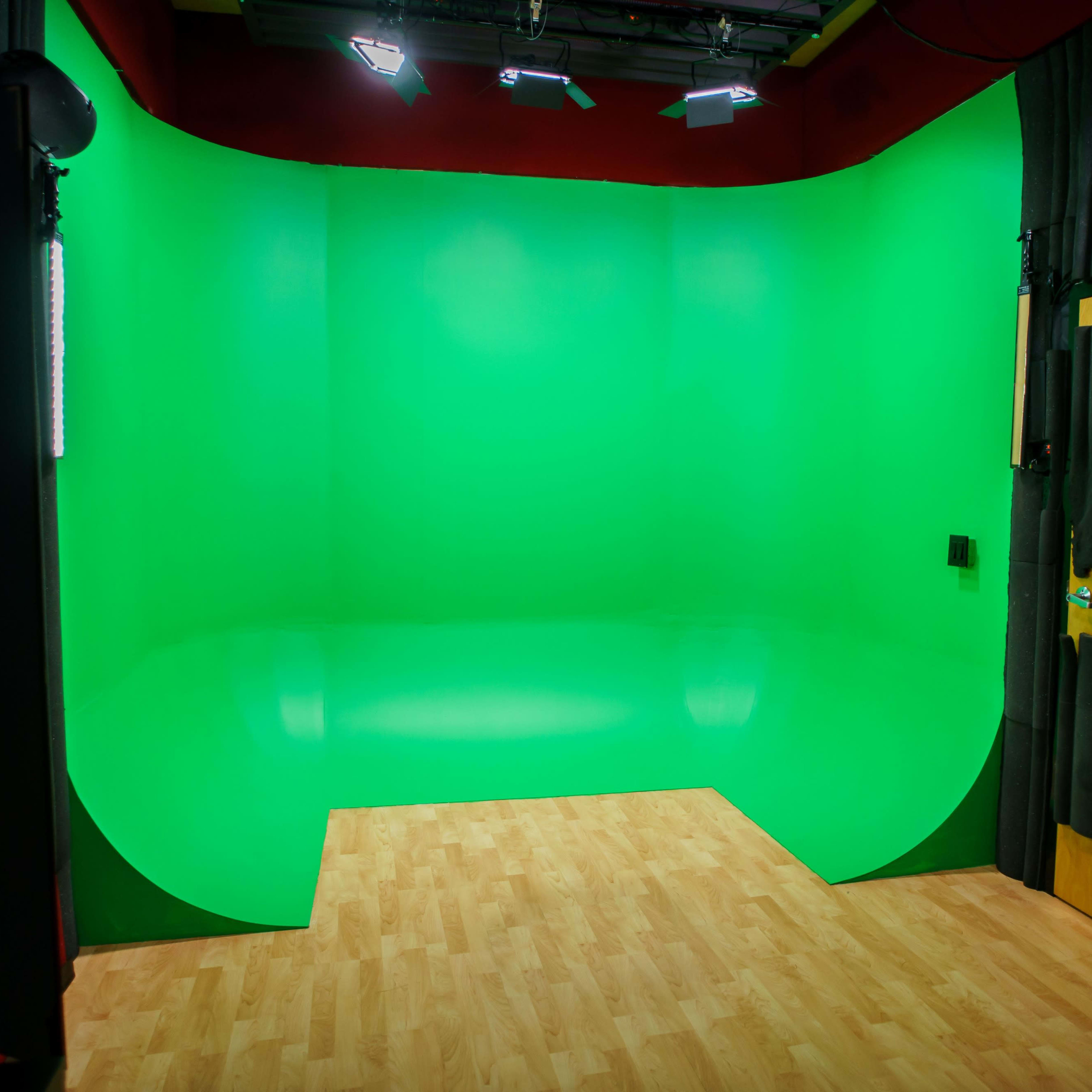 A green screen backdrop inside a studio, with wooden flooring and overhead lighting.