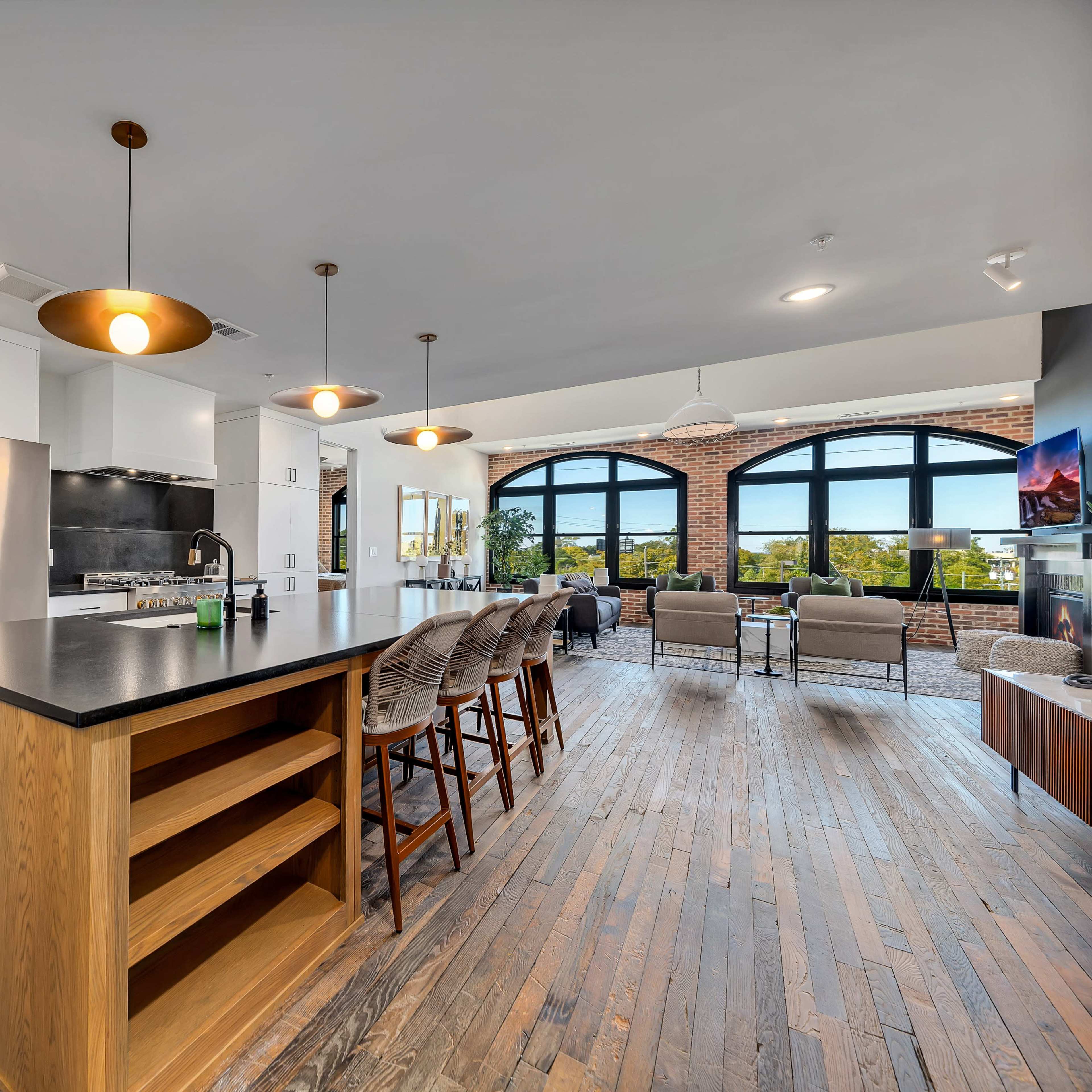 A modern kitchen and living area featuring an island with bar stools, stainless steel appliances, and large arched windows that provide natural light.