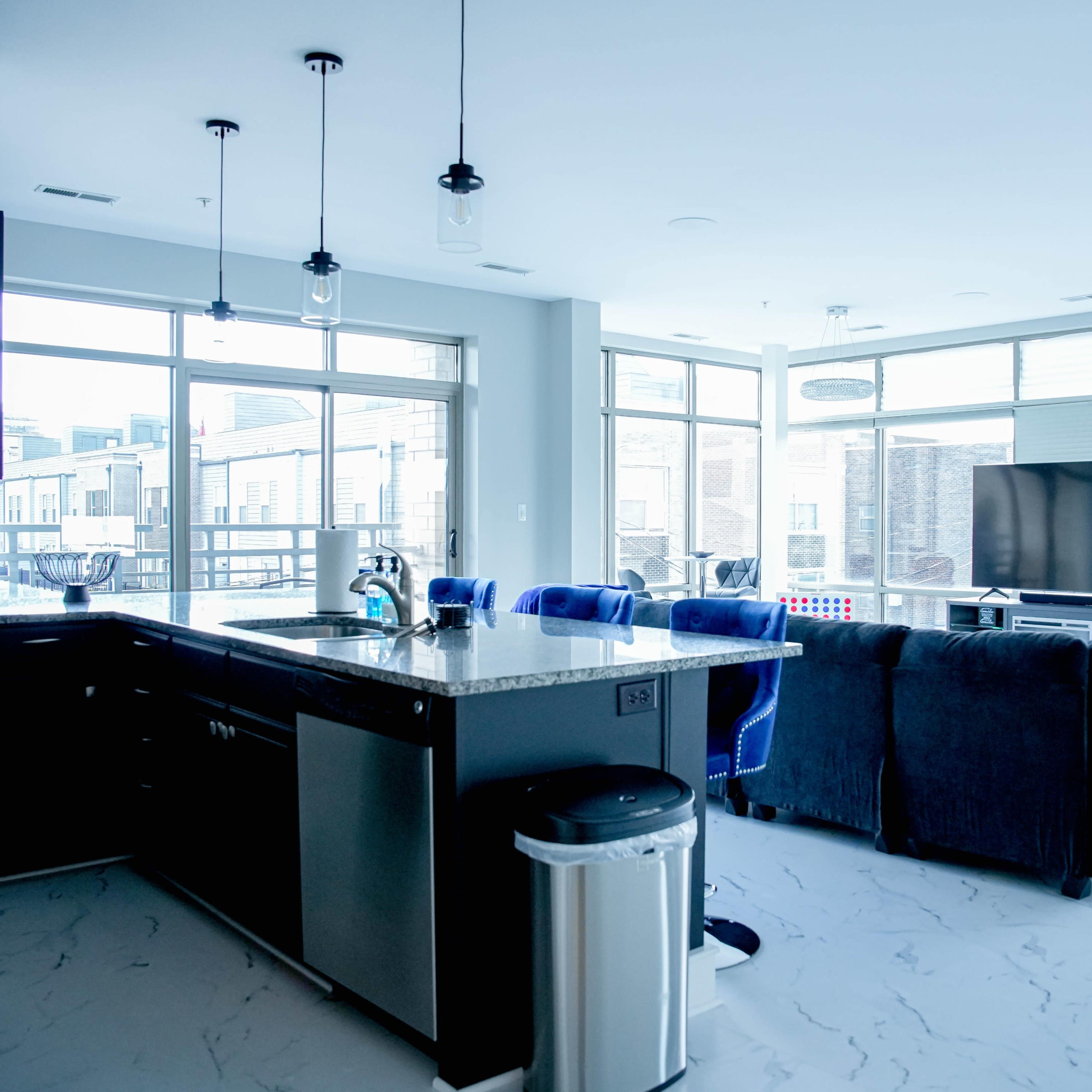 A modern open-concept living area with a kitchen, a large sectional sofa, and large windows overlooking an outdoor balcony.