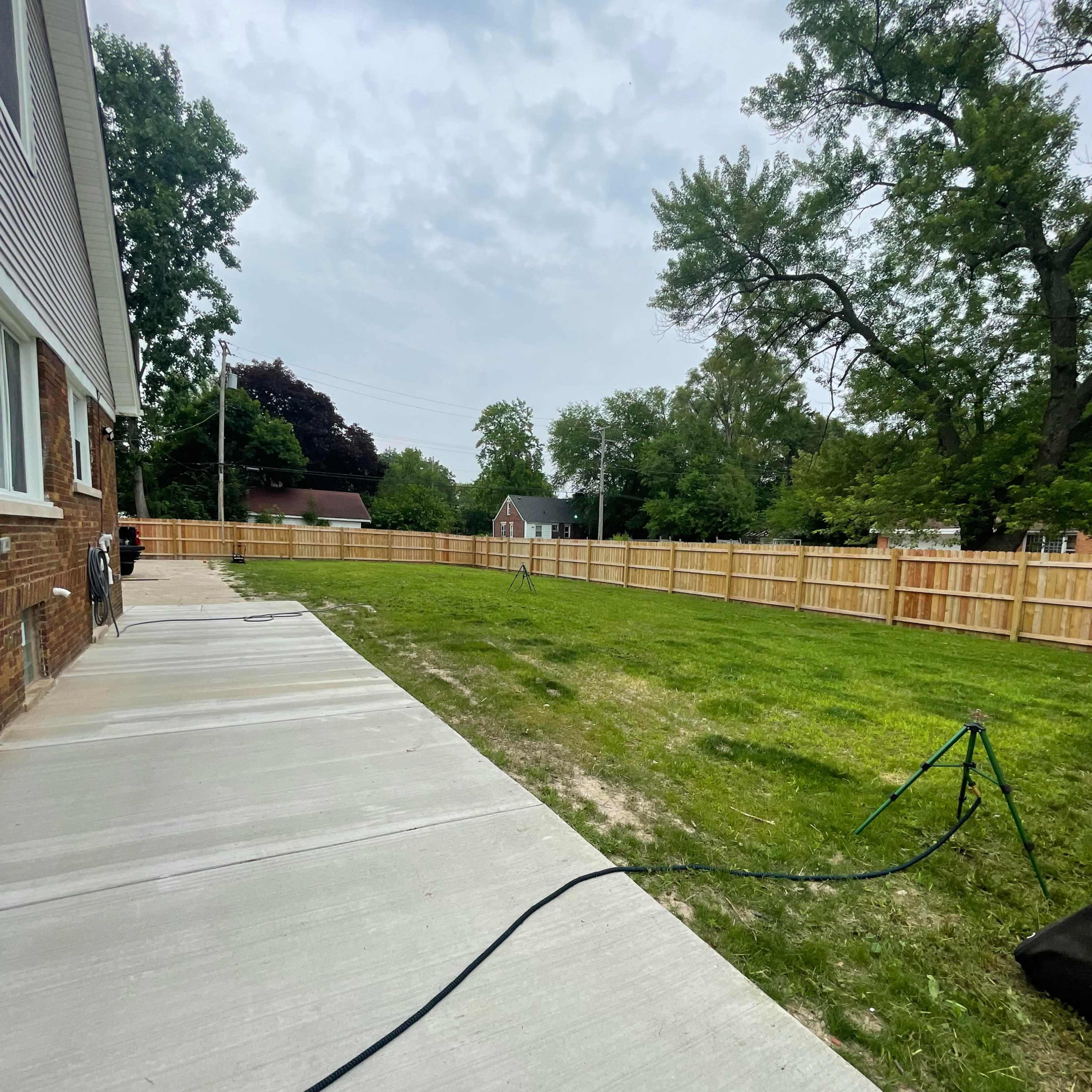 A grassy yard is enclosed by a wooden fence, with a concrete pathway leading to the house on one side.