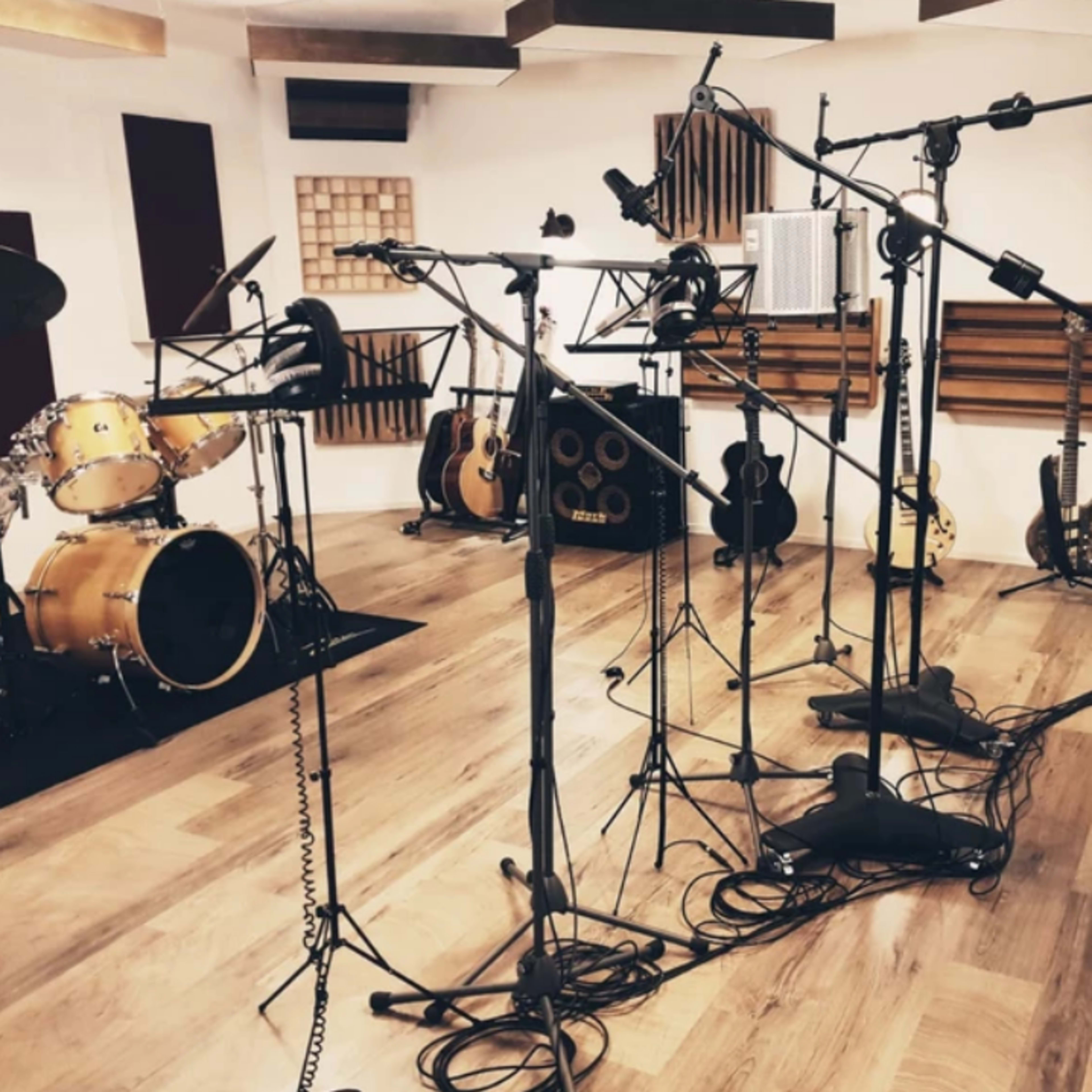 A recording studio with microphones setup around a drum kit and various musical instruments in the background.