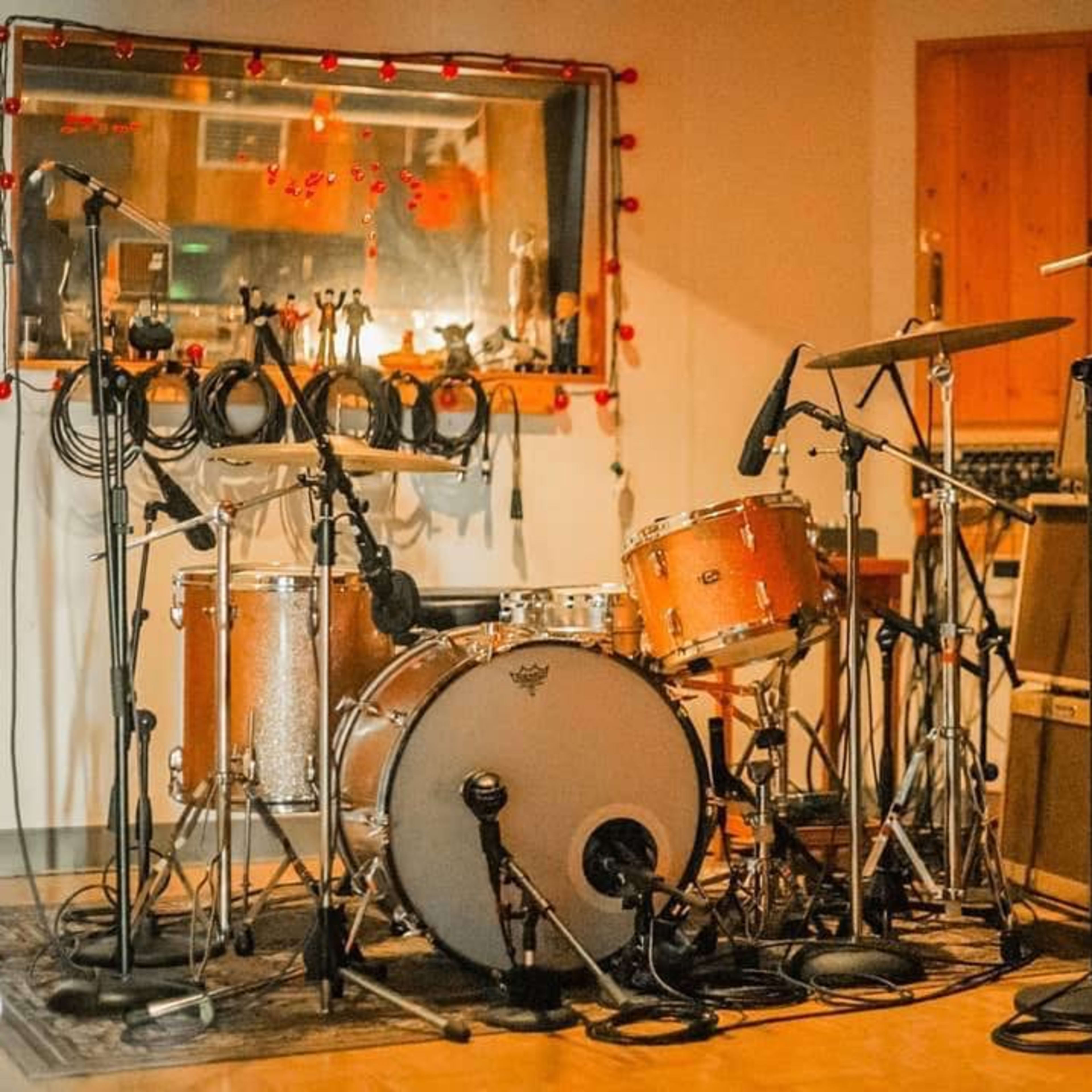 A recording studio with a vintage drum set positioned in front of amplifiers and microphones.