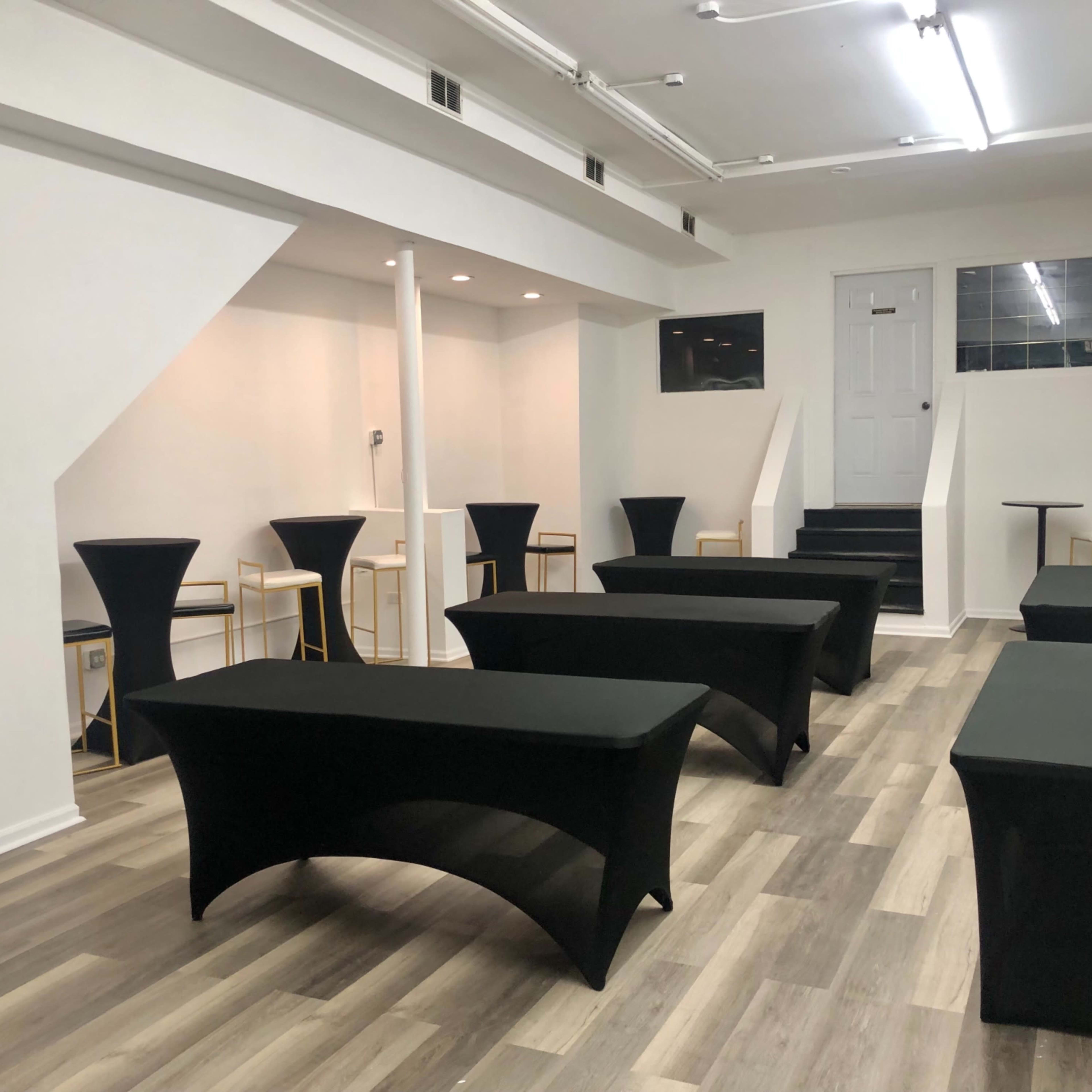 A spacious, empty room set up with several black-covered tables and a staircase at the far end.