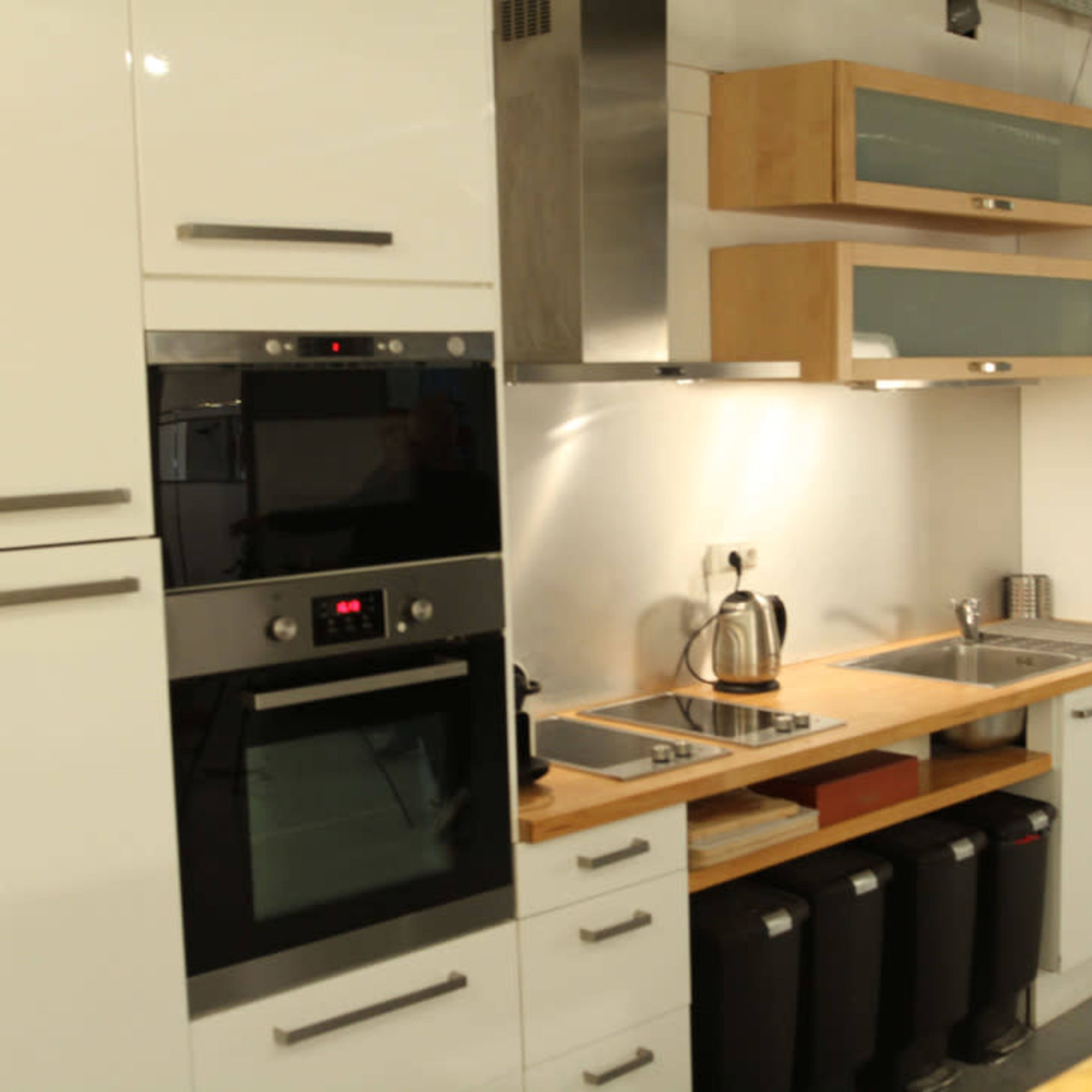 A modern kitchen with white cabinetry, stainless steel appliances, and a wooden countertop alongside a sink and garbage bins.