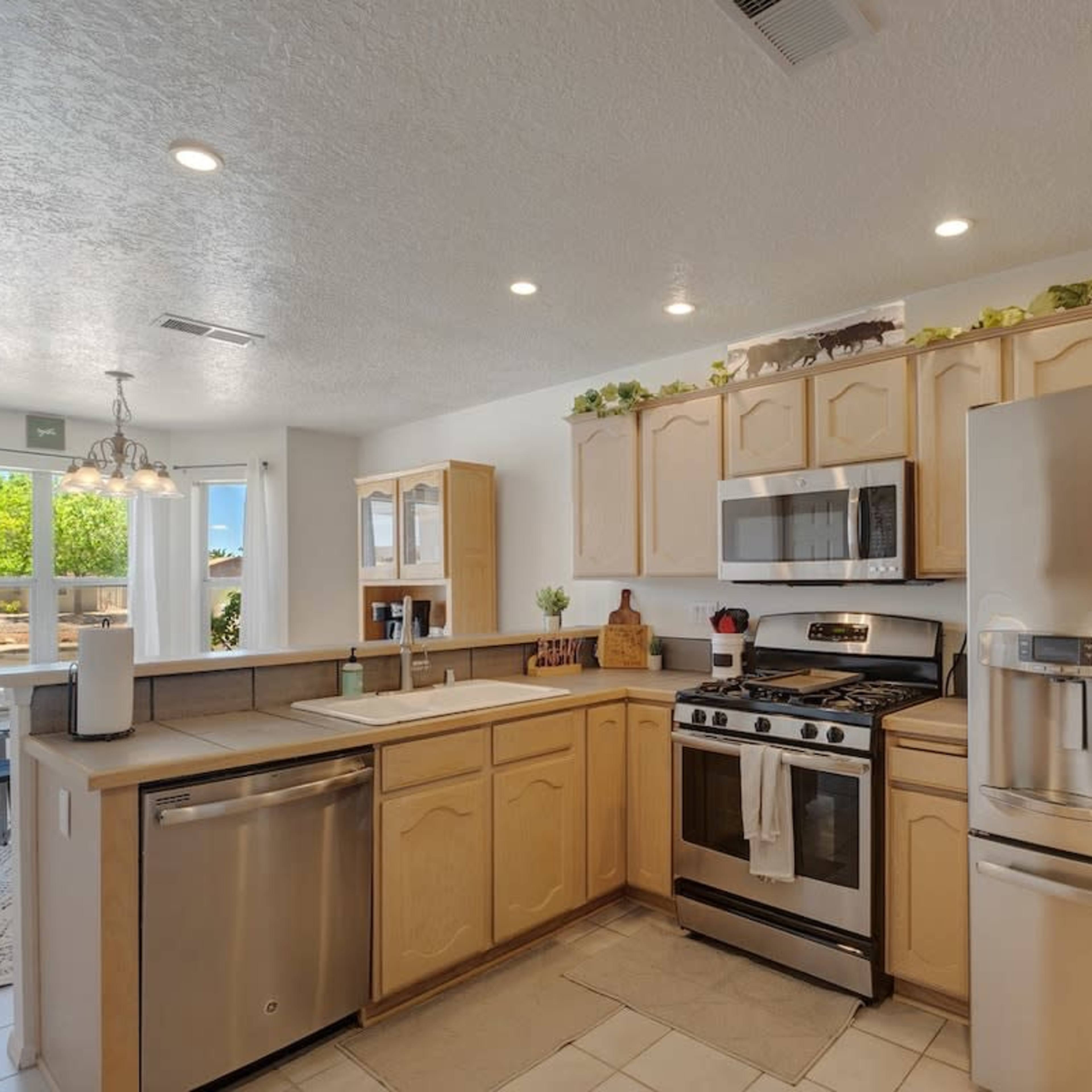 A modern kitchen features light wood cabinetry, stainless steel appliances, and a spacious layout with a view of the outdoors.