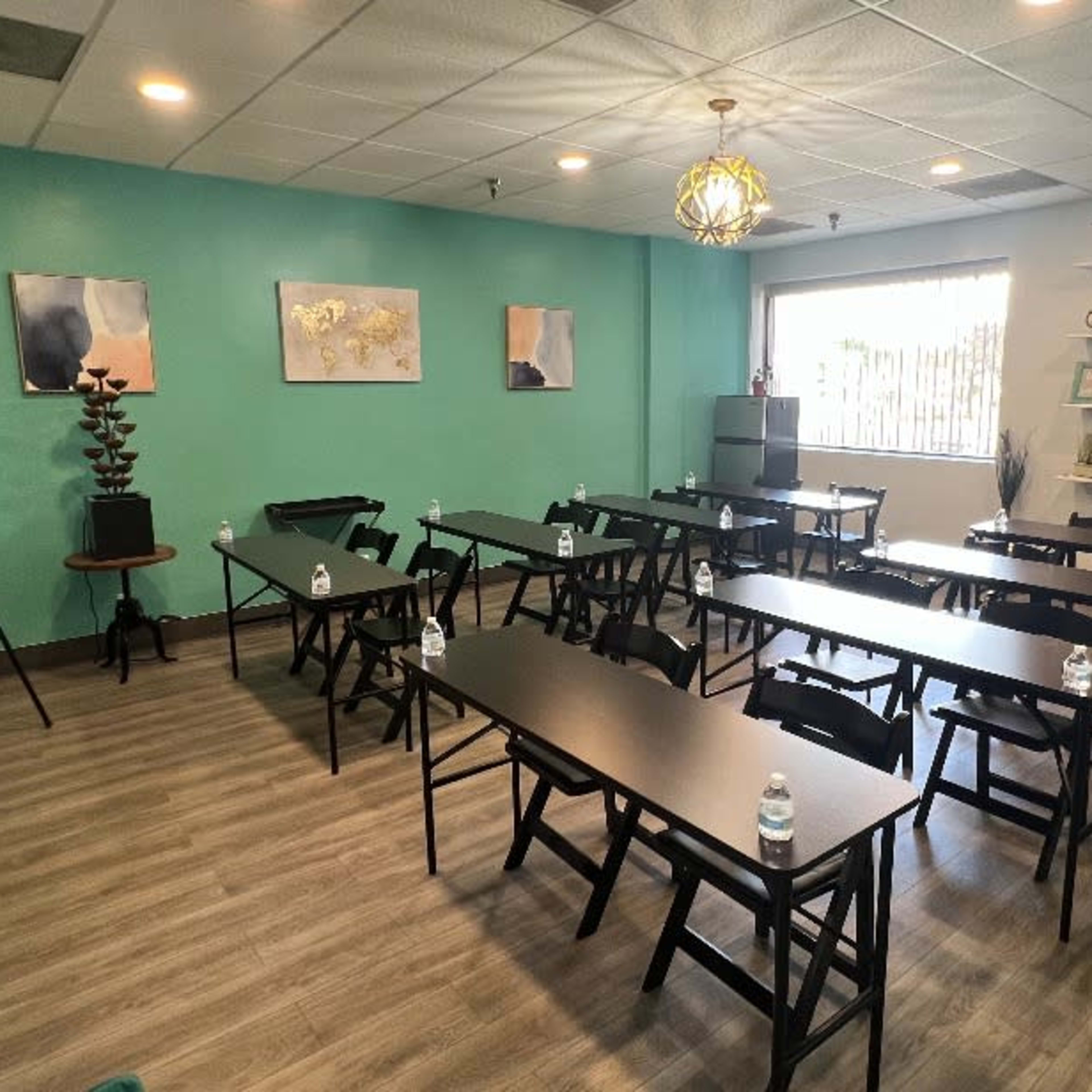 A well-arranged classroom with several black tables and chairs, a green accent wall, and decorative shelves filled with various items.