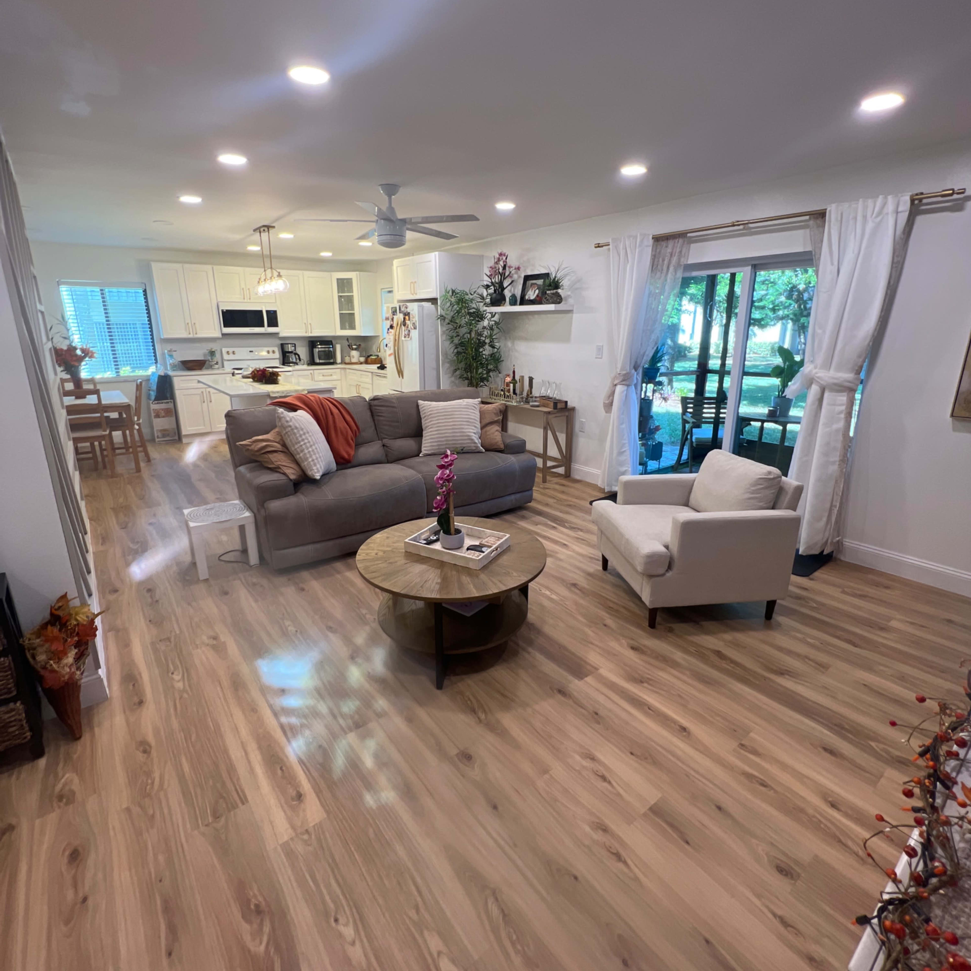 A modern living room with a gray sofa and a white armchair, a round coffee table, and large windows providing natural light.